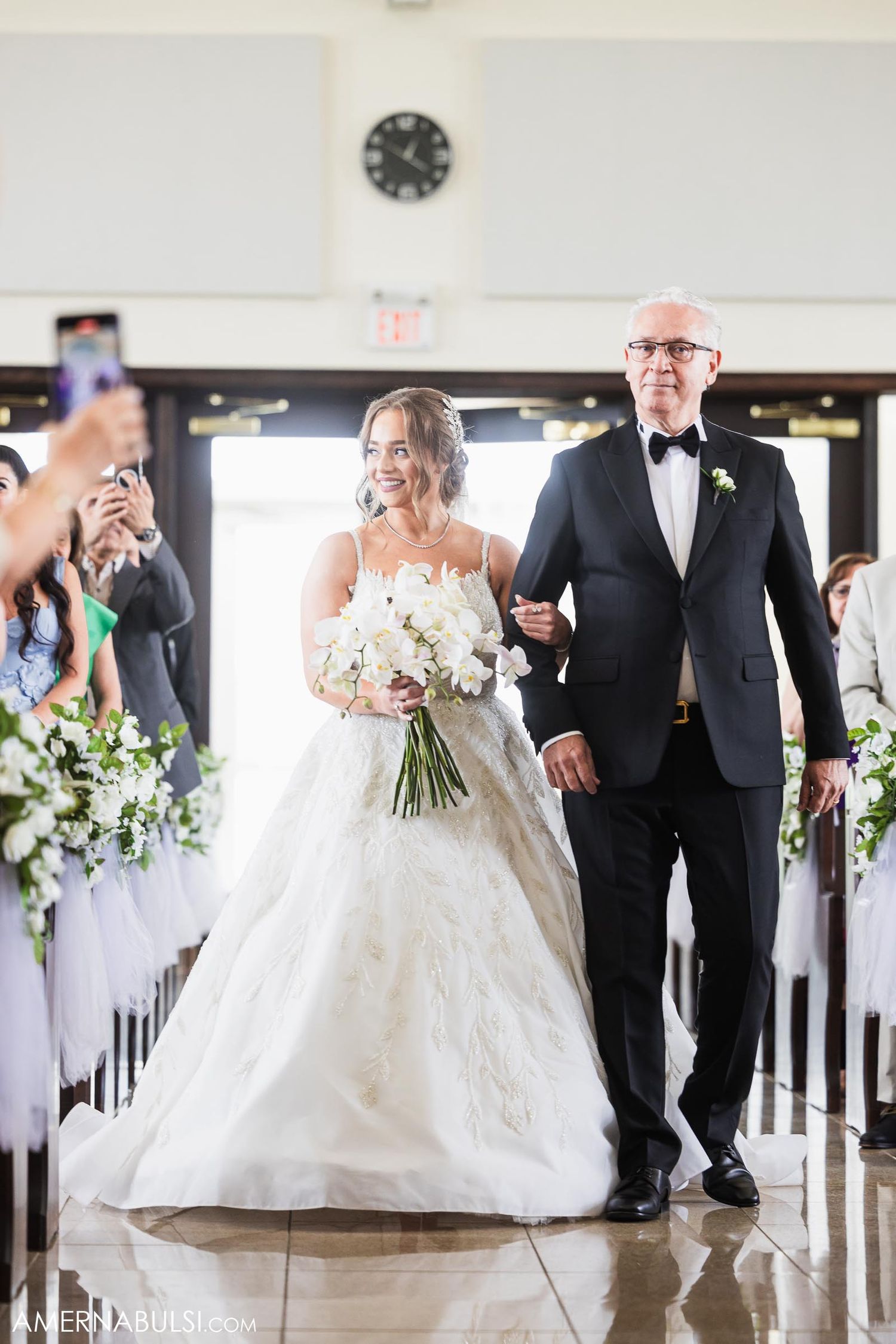 Bride in white gown walking down aisle with father during traditional church ceremony.