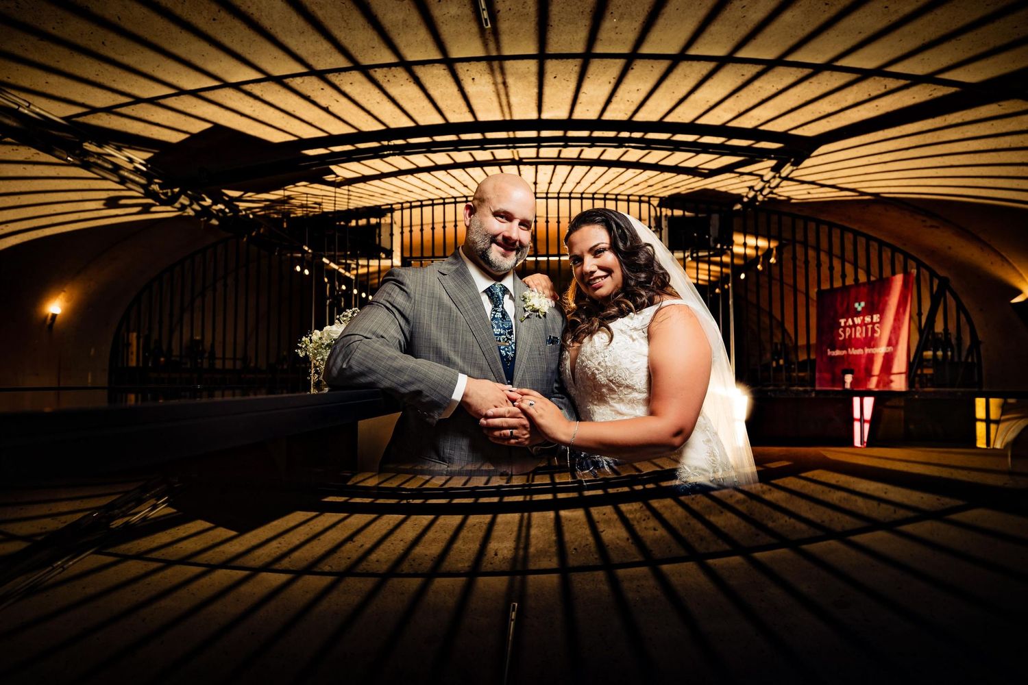 Creative wide-angle wedding portrait under ornate architectural ceiling with warm lighting.