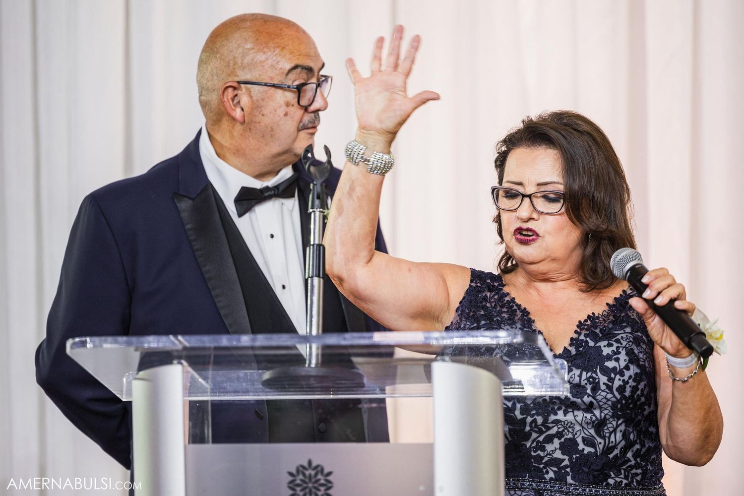 Two people speaking at a wedding reception podium with animated expressions.