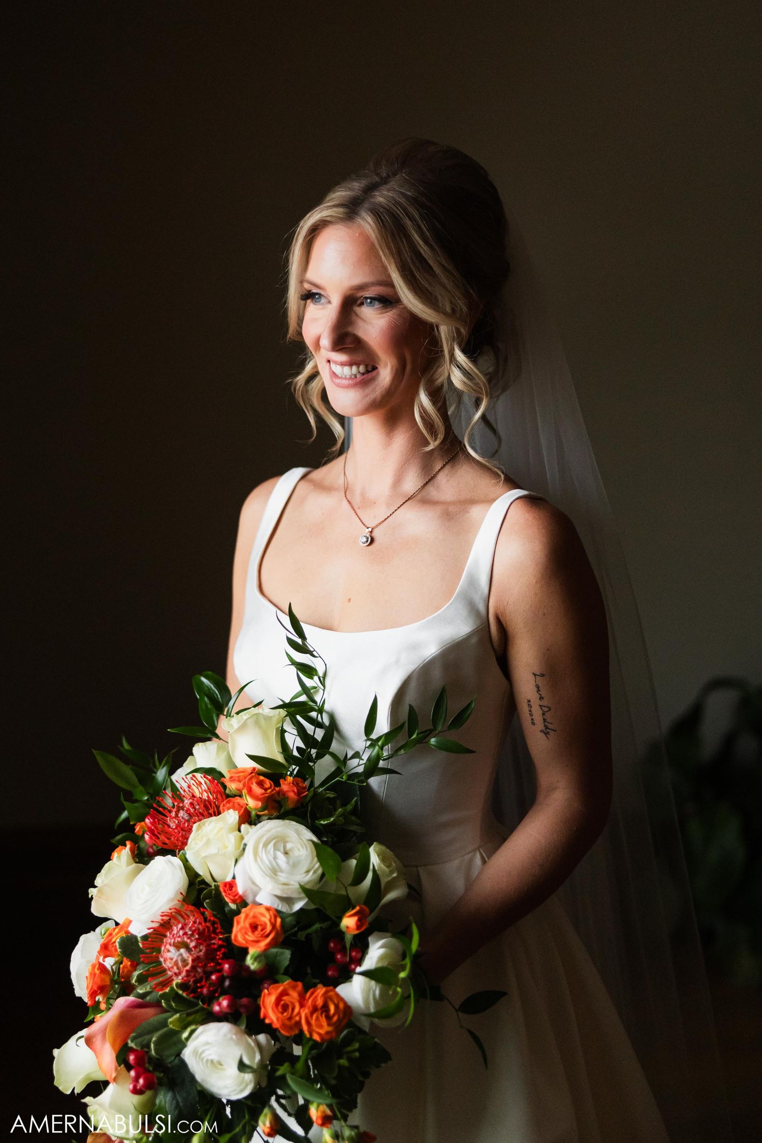 A bride holds a lush bouquet of coral and white flowers against a dark background.