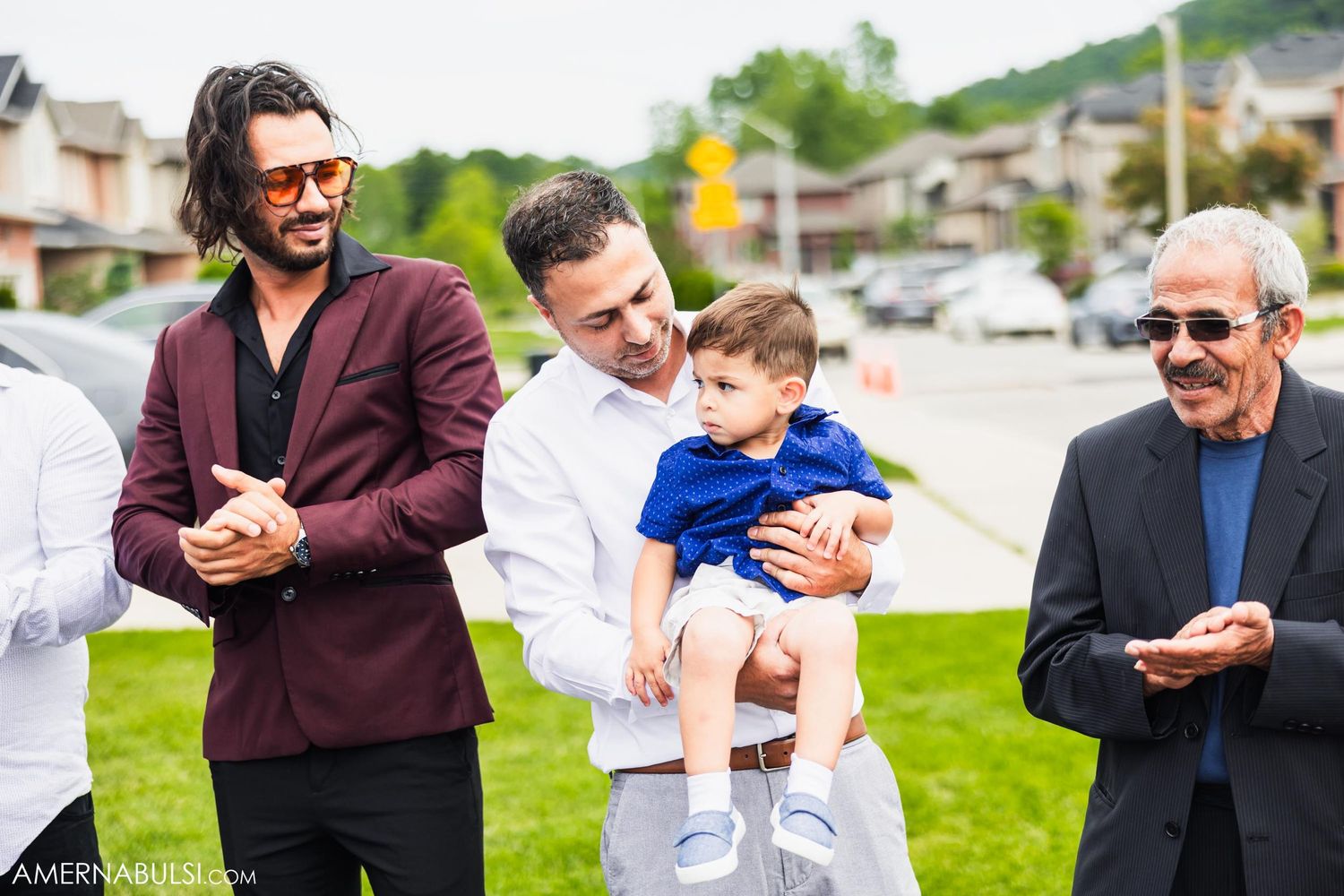 Wedding guests smile and hold a young child during outdoor celebration.