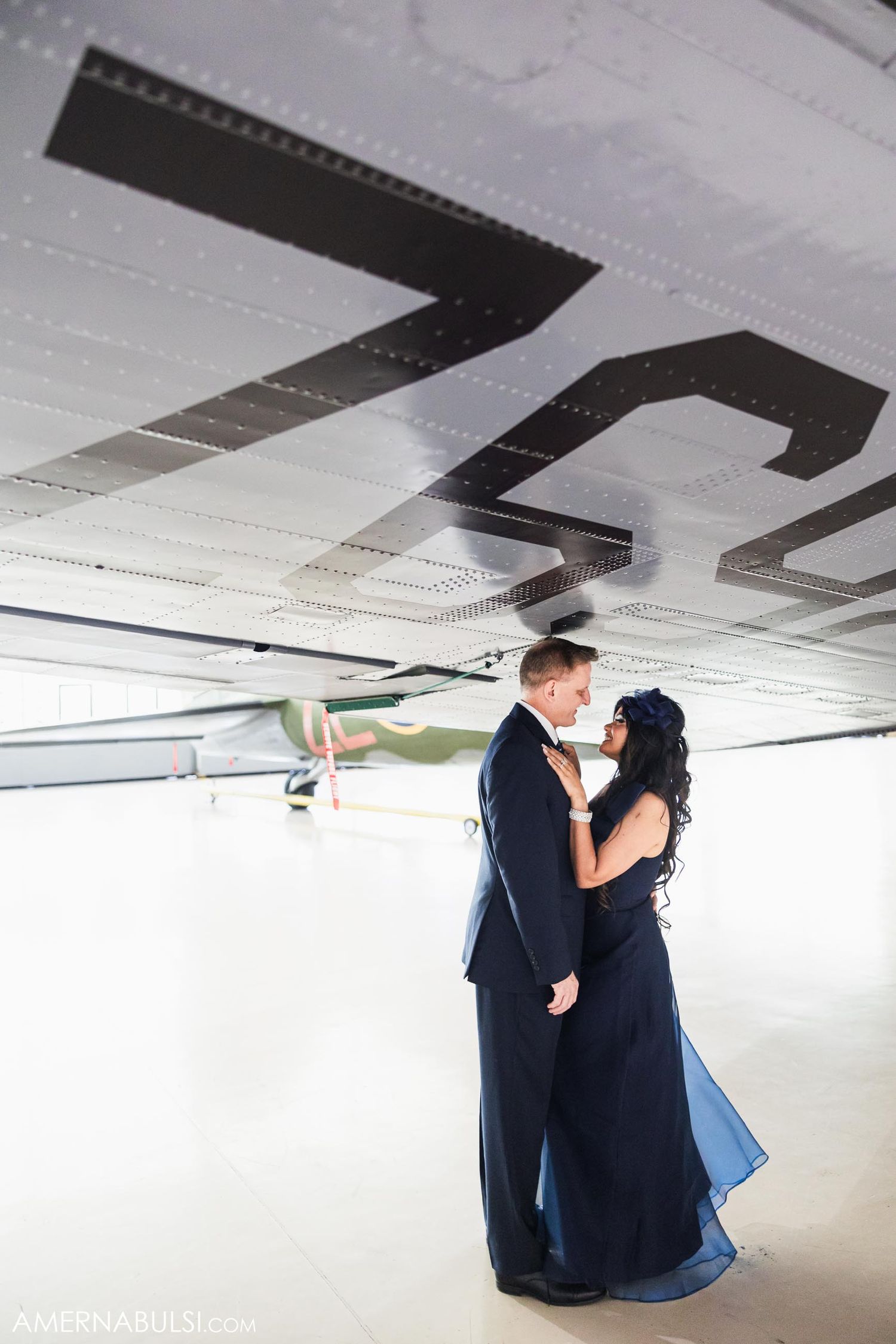 Romantic couple embracing beneath aircraft wing with geometric patterns.