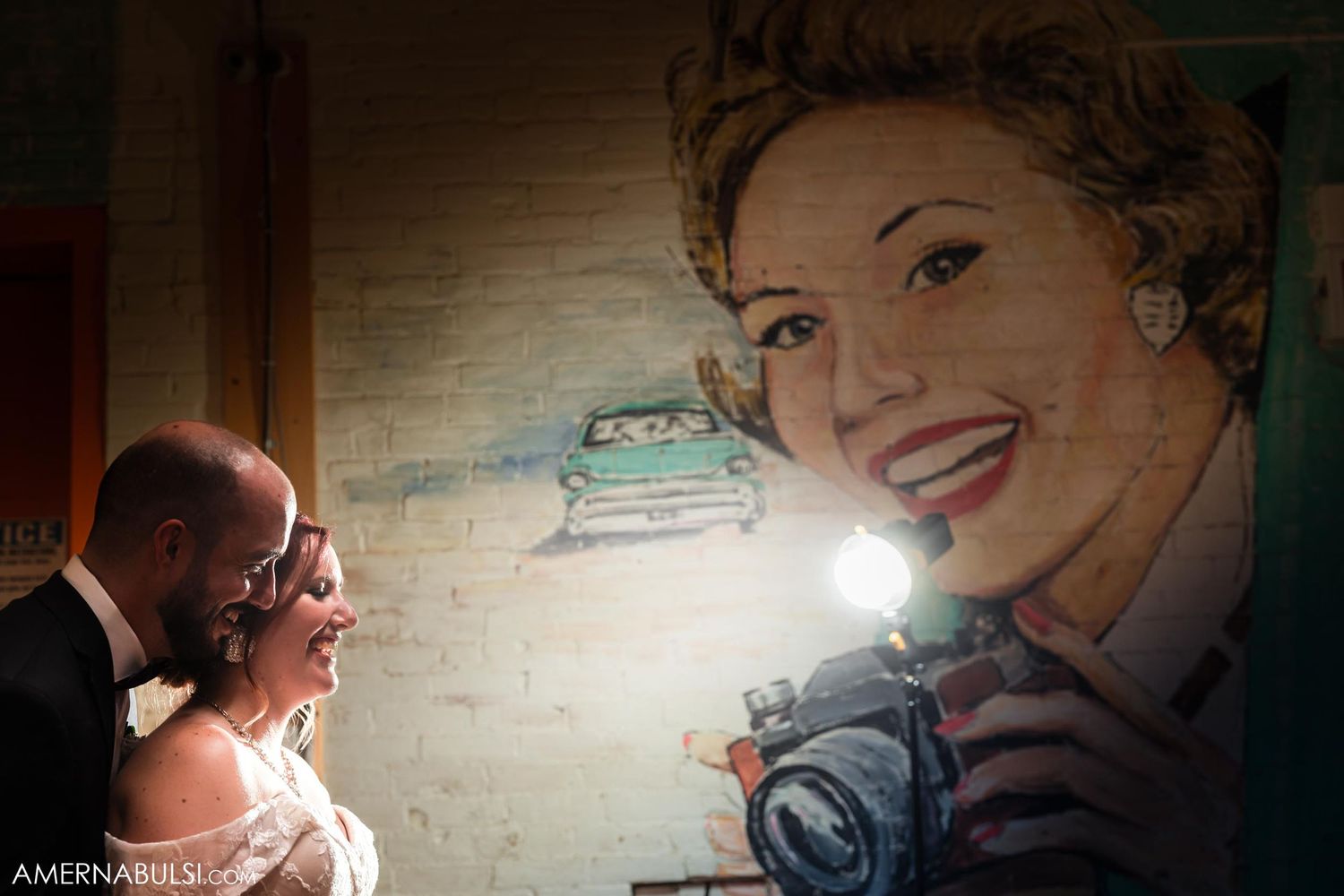 Wedding couple poses near vintage-style wall mural with dramatic lighting.