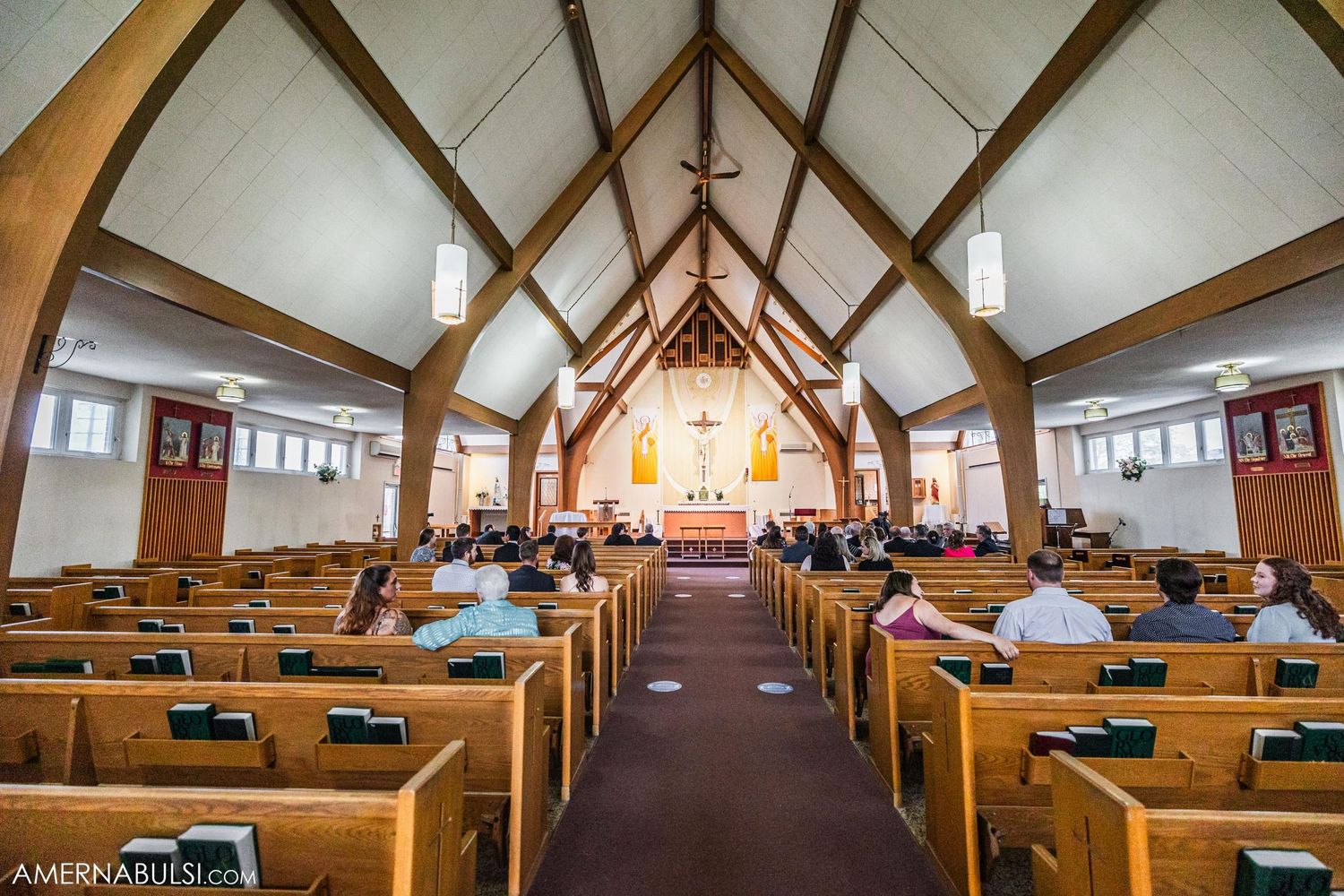 Interior of a traditional church with vaulted wooden beams, rows of pews, and an illuminated altar.