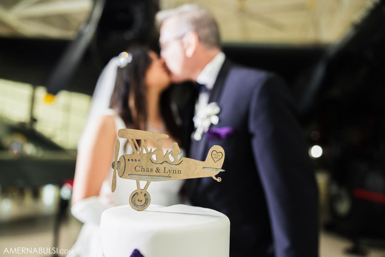 Decorative wooden airplane cake topper with blurred wedding scene in background.