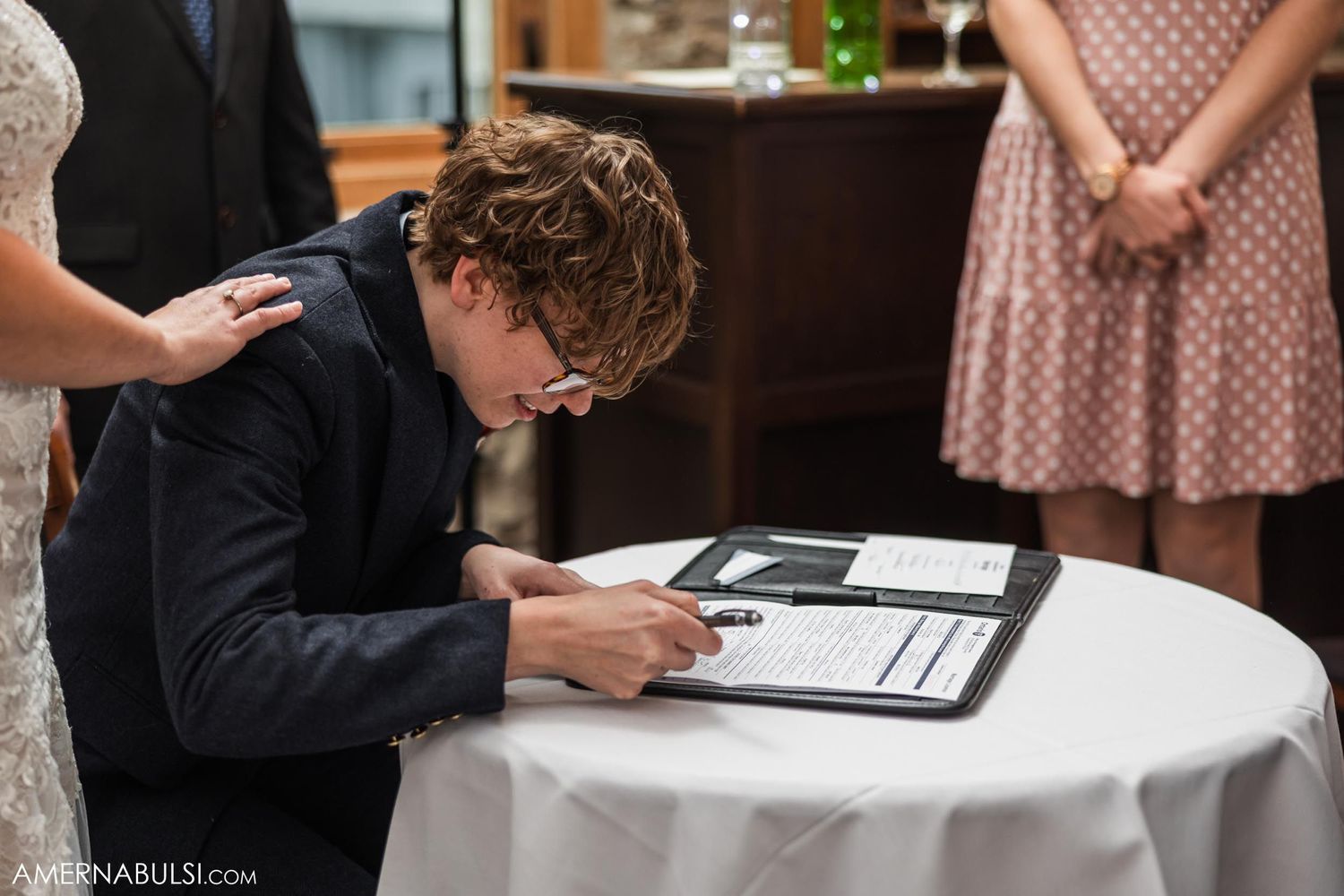 Person in formal attire signs marriage documents at round table.