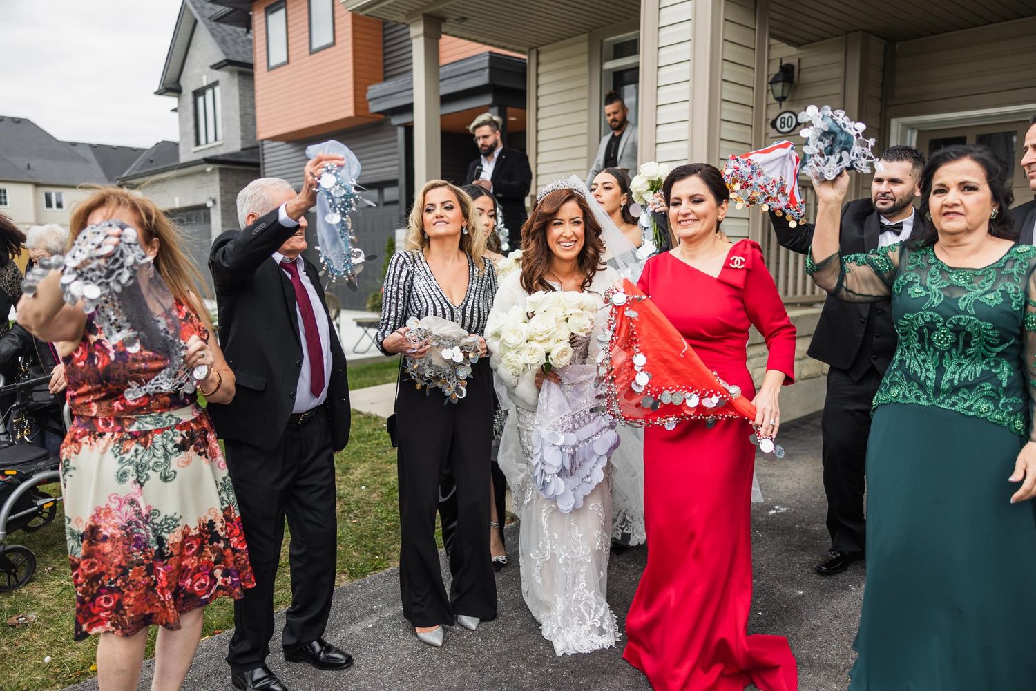 Wedding party members in formal attire pose together on a front porch.
