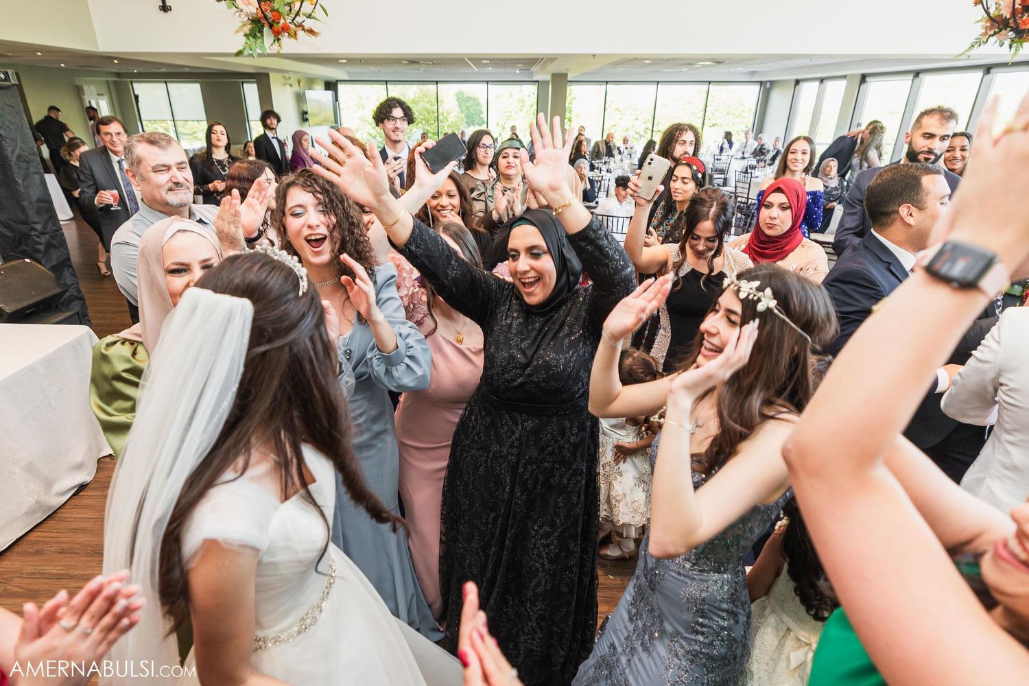 Wedding reception guests dancing and celebrating with joy in a bright indoor venue.