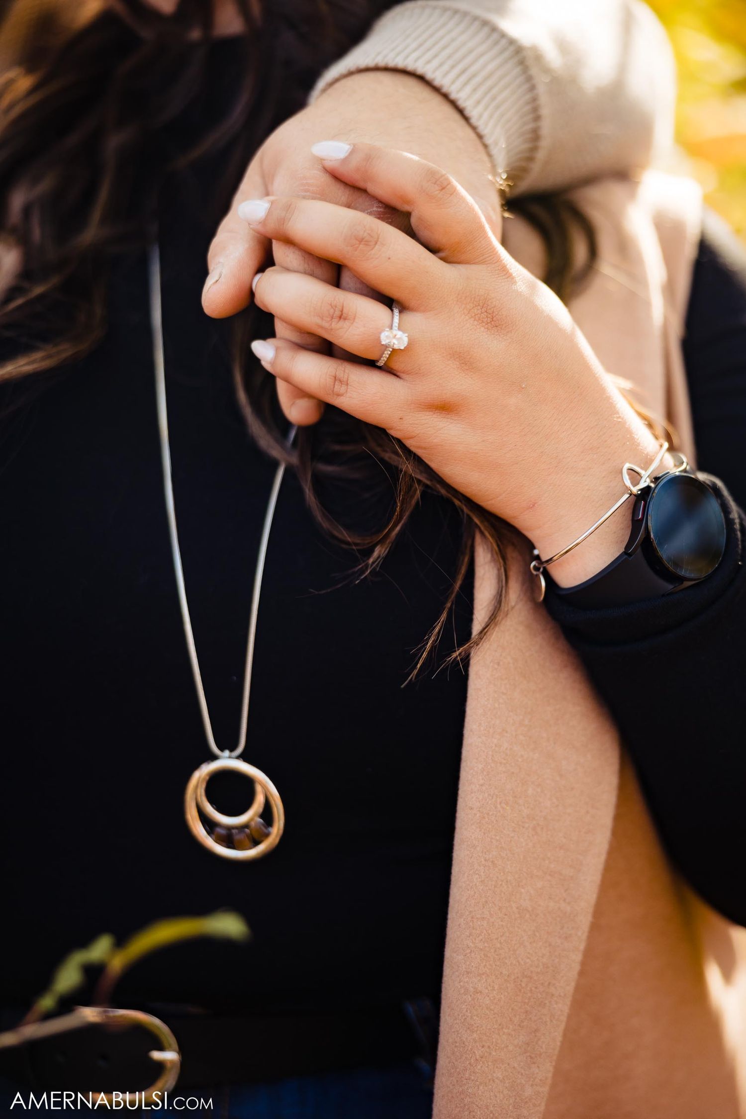 Close-up of engagement ring and necklace jewelry details against black sweater.