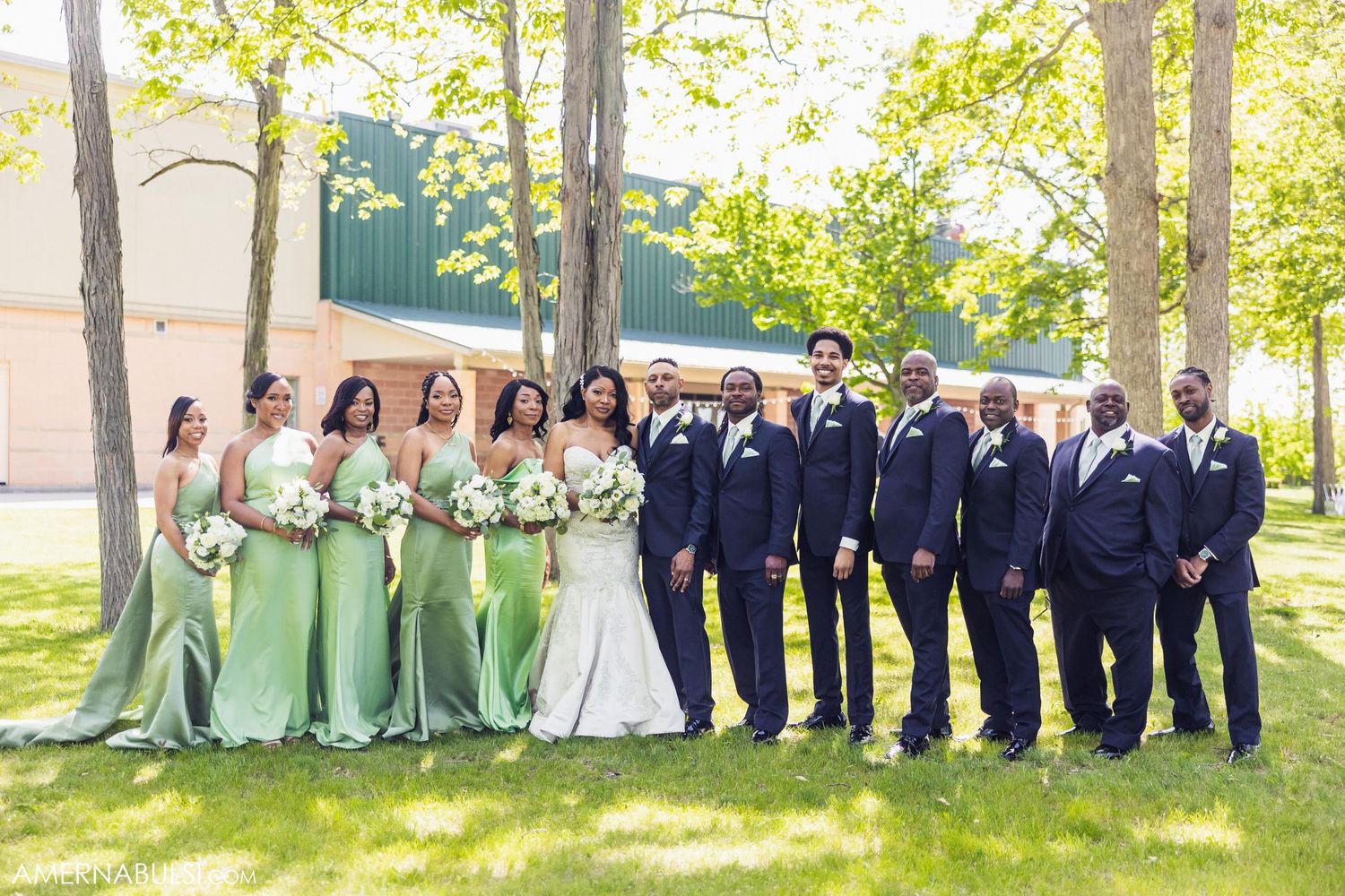 Wedding party in navy suits and mint green dresses poses together on sunny spring day.