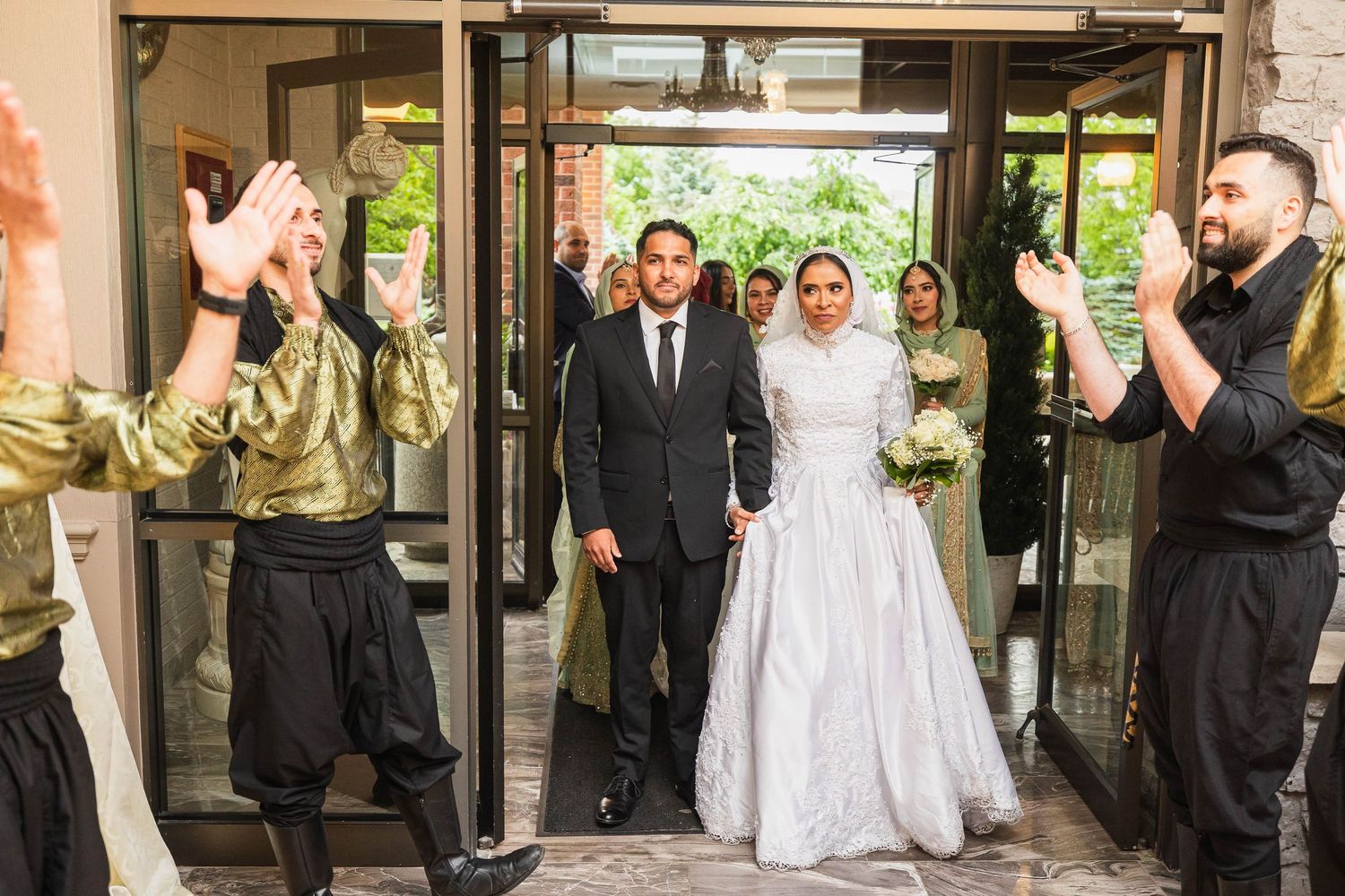A joyous wedding celebration as guests cheer while a couple exits through glass doors.