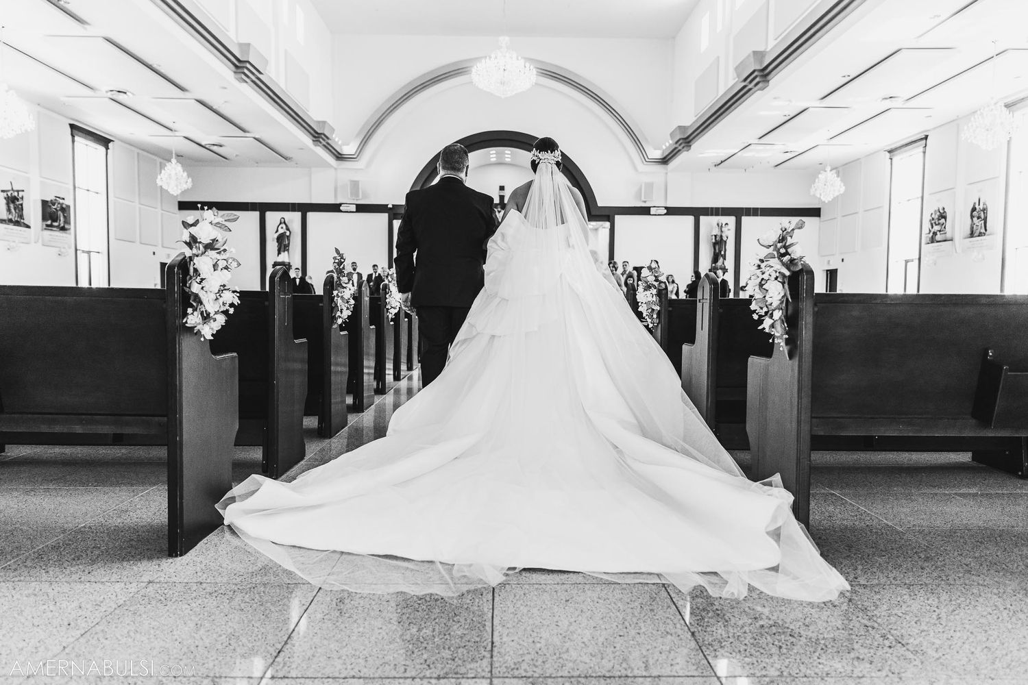 A dramatic black and white photo of a bride's wedding dress train in a church aisle.