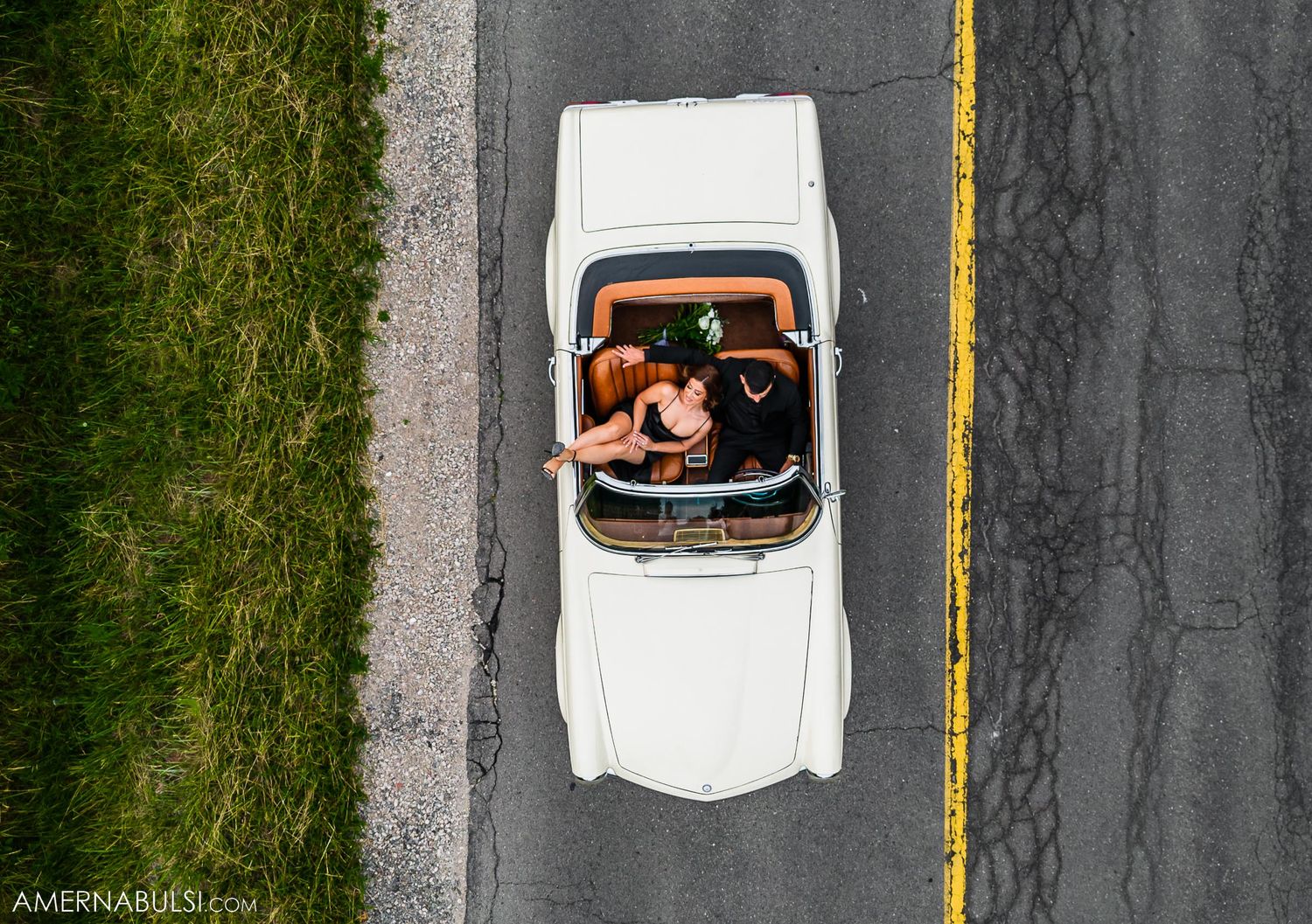 Aerial view of couple in vintage white Mercedes-Benz convertible on rural road.