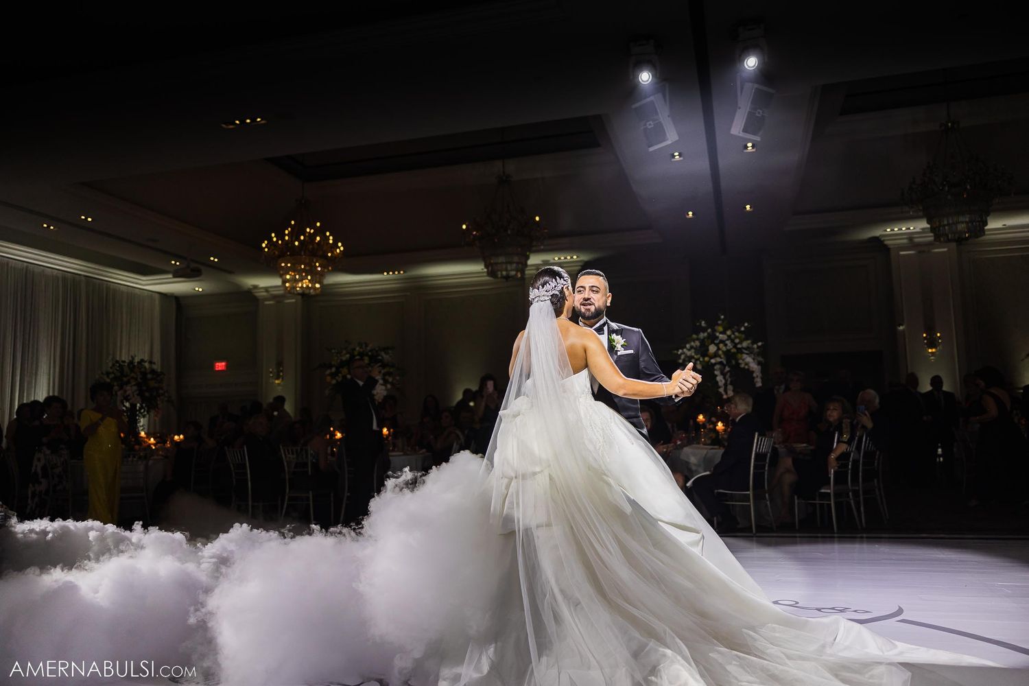 Couple shares first dance on misty dance floor under dramatic lighting.
