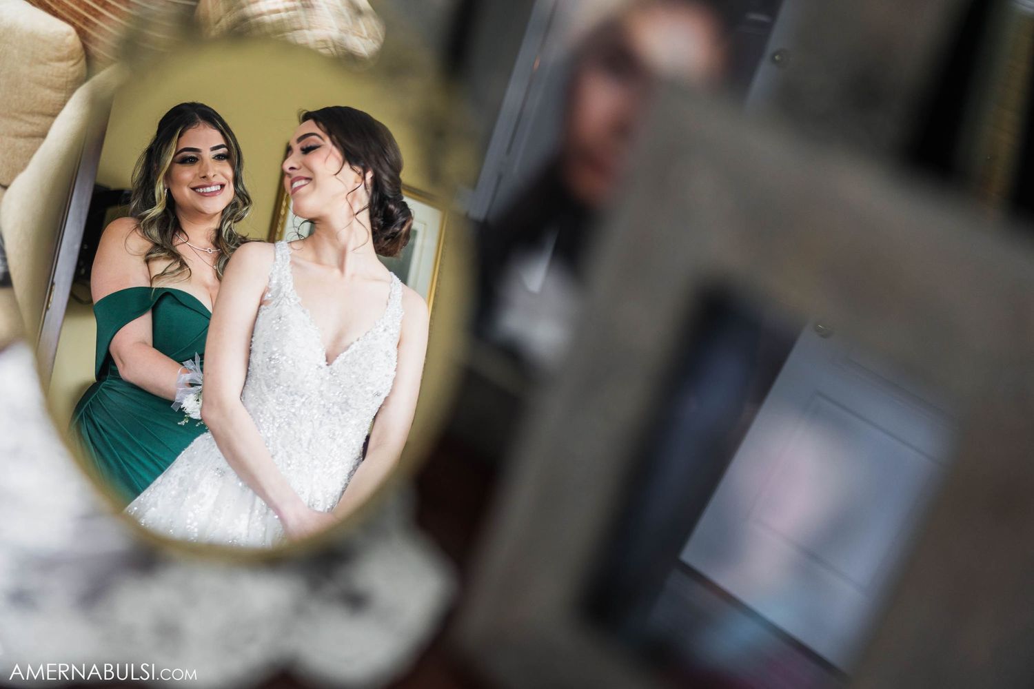 Two friends share a joyful moment reflected in an antique mirror during wedding preparations.
