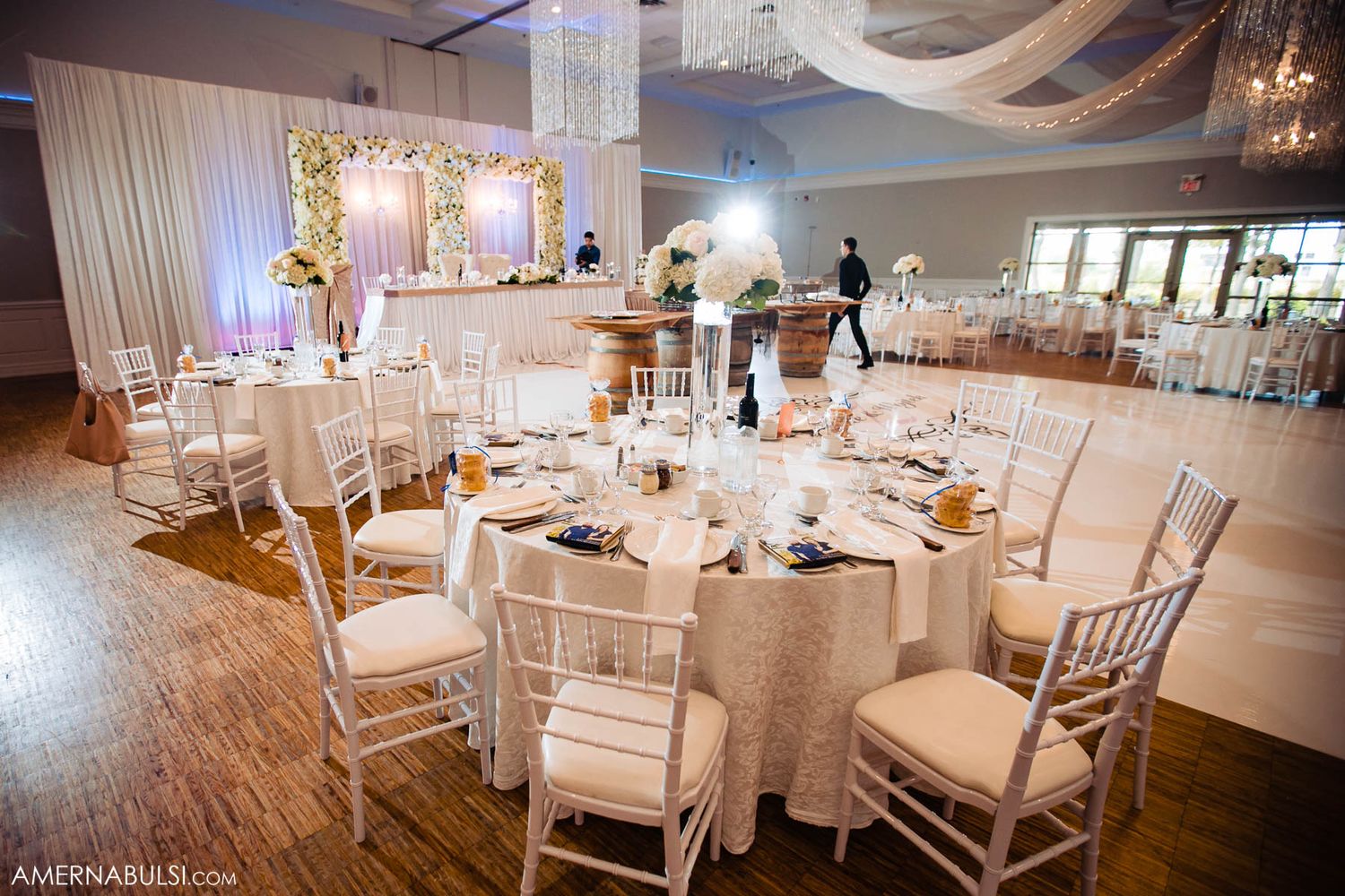 Elegant wedding reception venue with white chairs and tables set for dining under soft lighting.