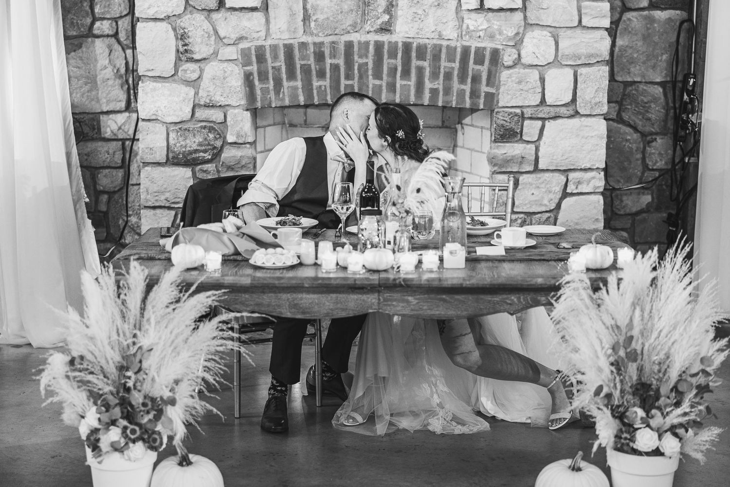 A romantic moment captured in black and white near a rustic stone fireplace with pampas grass decor.
