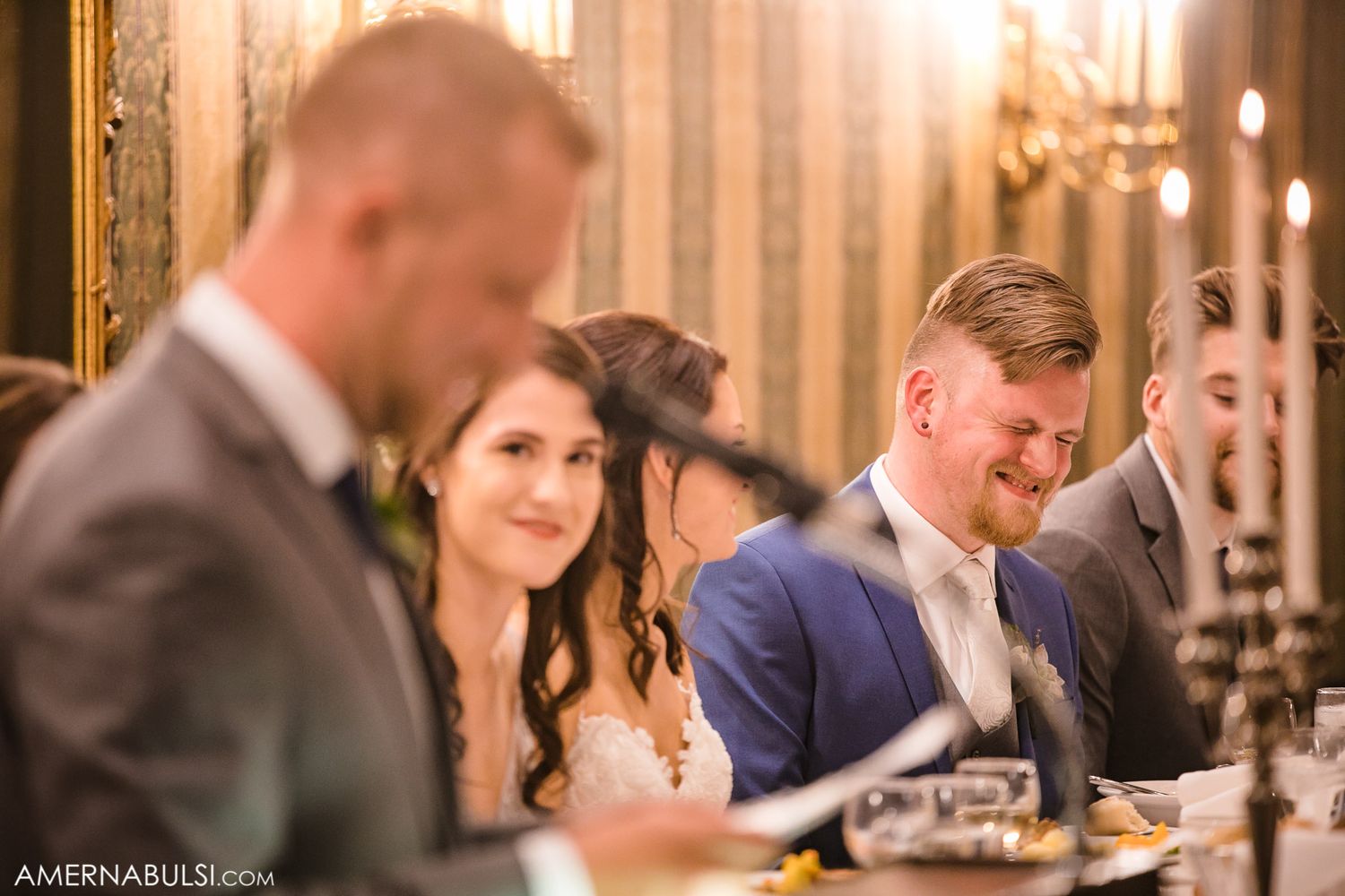 Wedding reception guests seated at tables with candlelight and formal place settings.