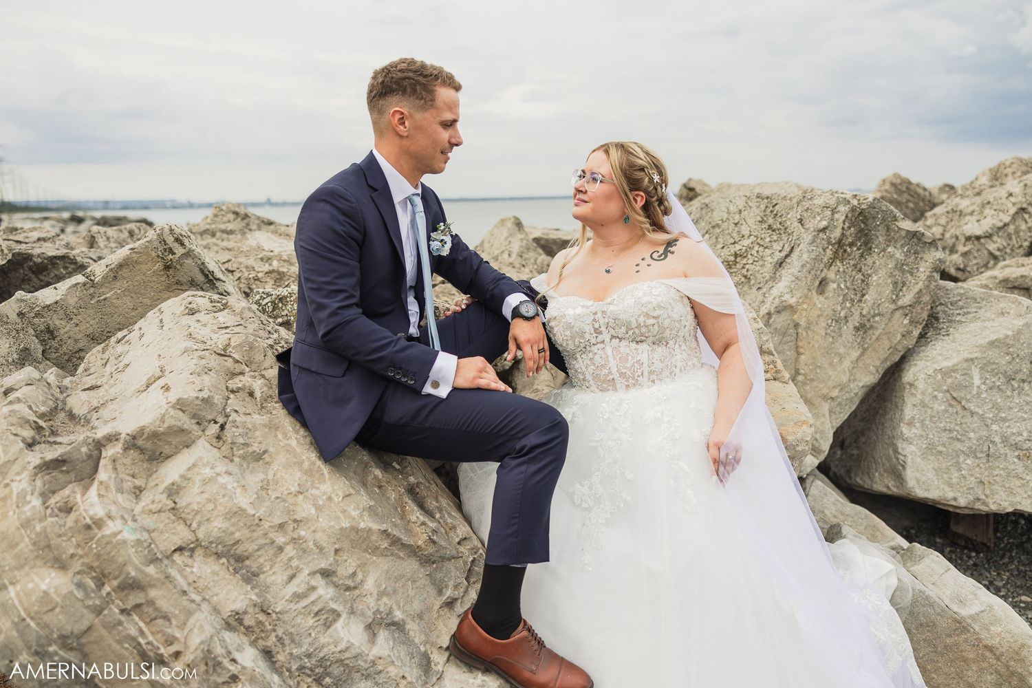 Newlyweds posing on rocky coastal outcrop in formal wedding attire.