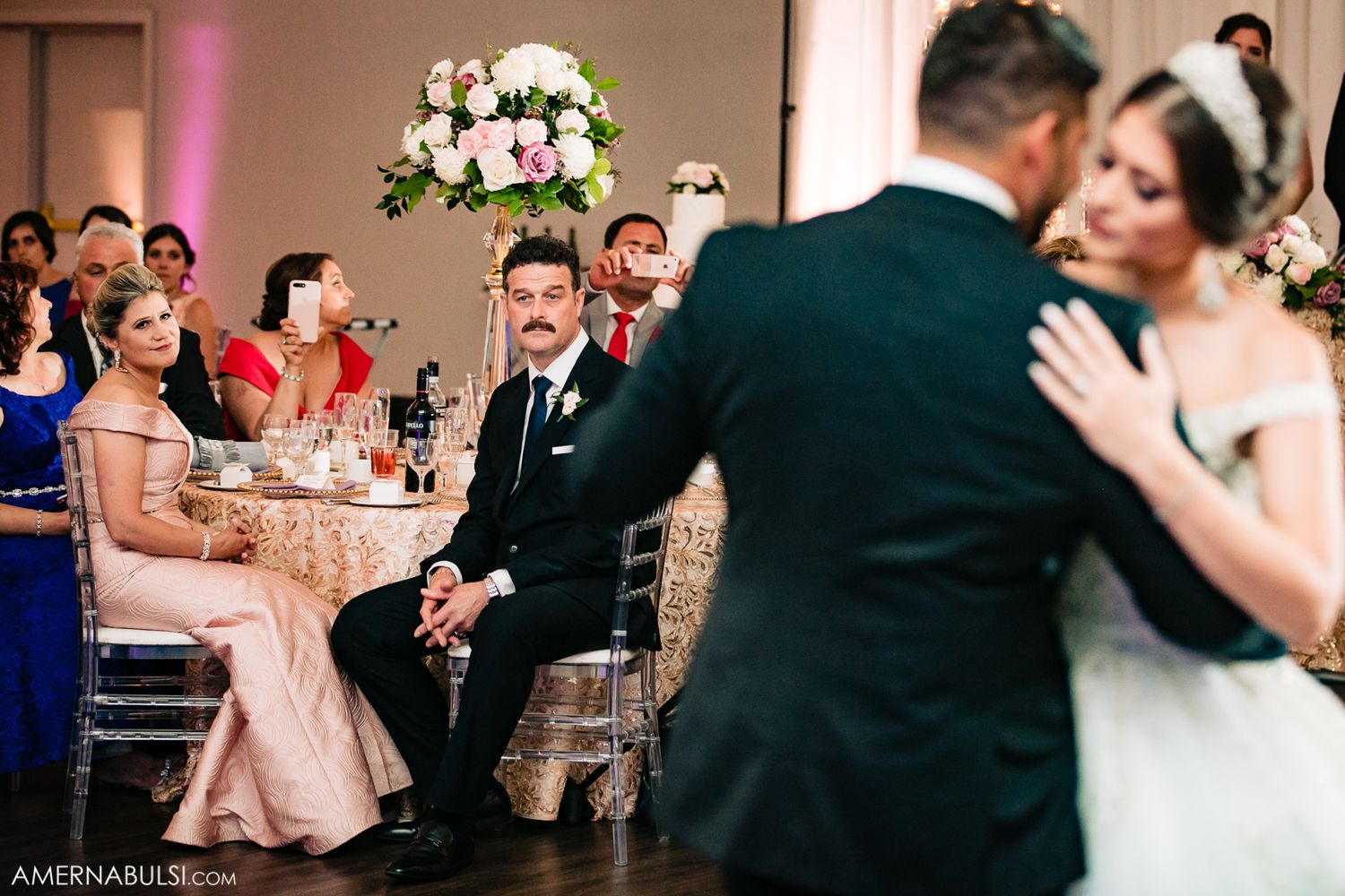 Couples dancing together at an elegant wedding reception with floral centerpieces visible in the background.