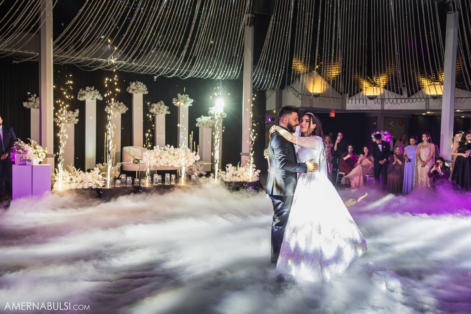 A wedding couple dances surrounded by dramatic low-lying fog effects on an illuminated dance floor.