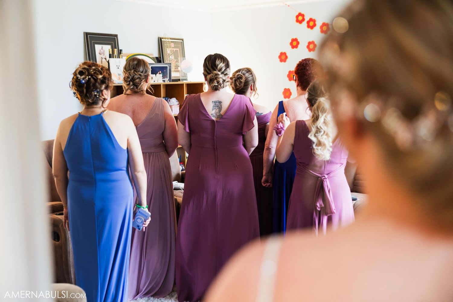 Wedding party wearing purple and blue dresses gathered in a bright room.