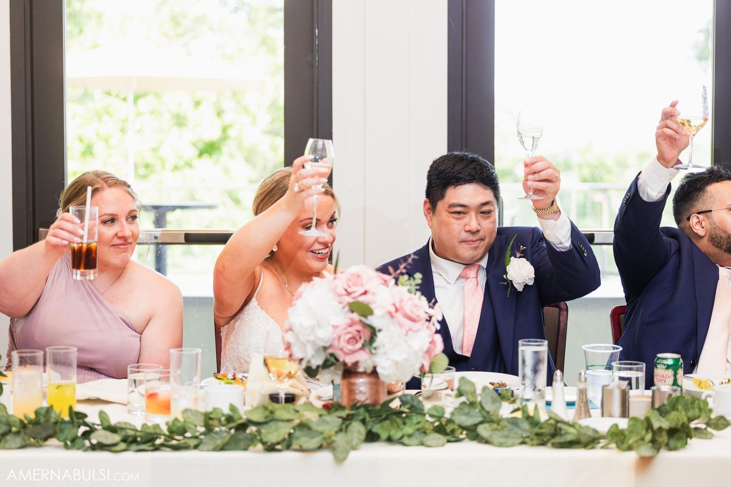 Wedding party members raise their glasses in a celebratory toast at the head table.
