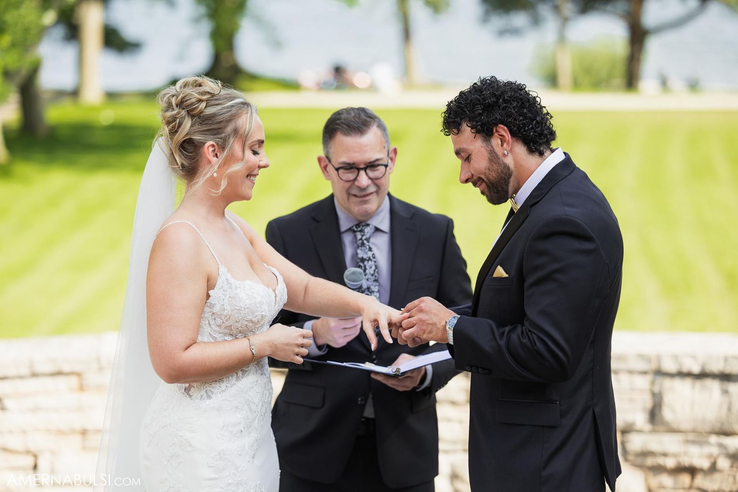 Outdoor wedding ceremony showing couple exchanging vows with celebrant on sunny day.