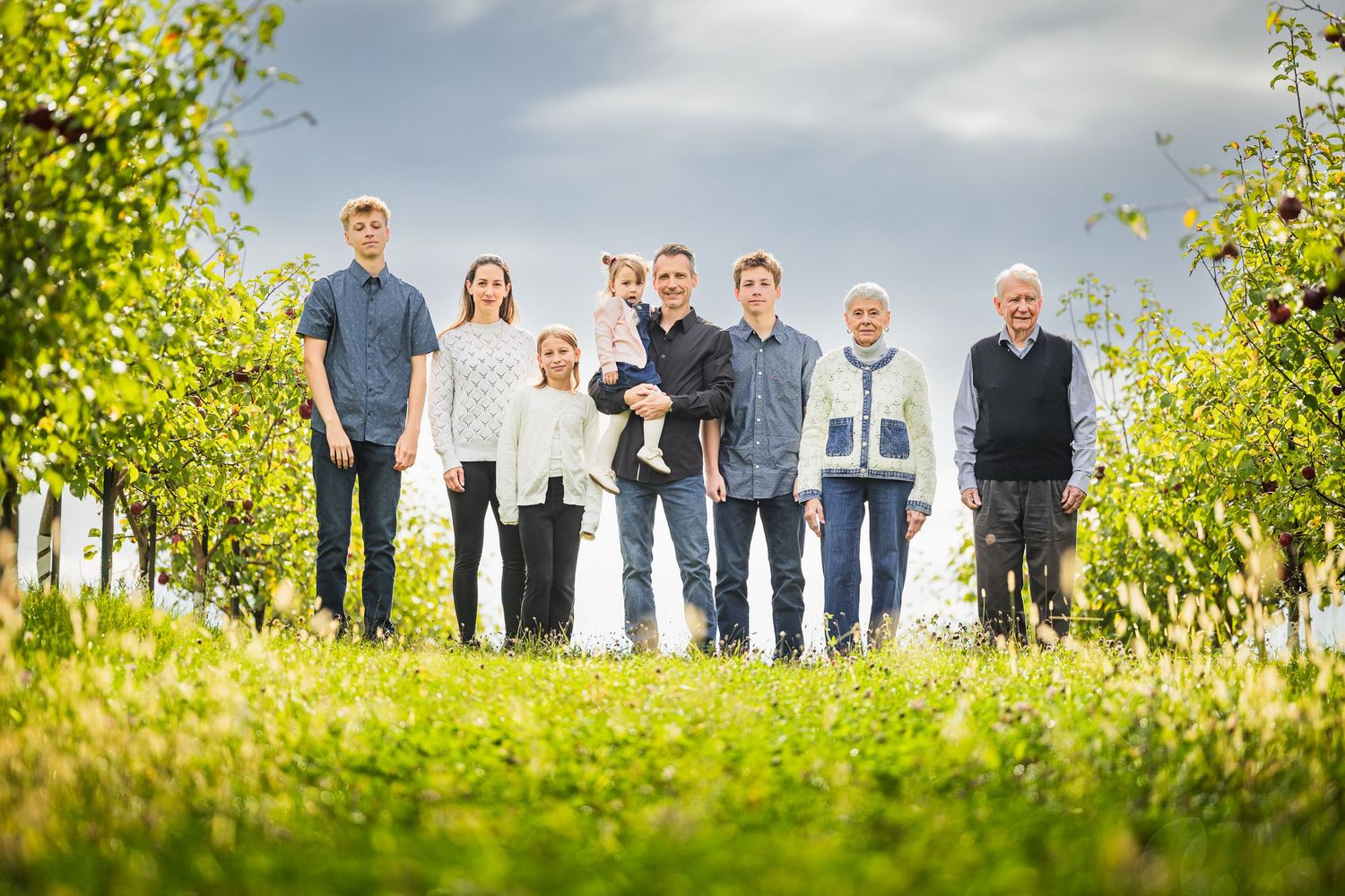 A group of people stand together in a sunny apple orchard on a bright autumn day.