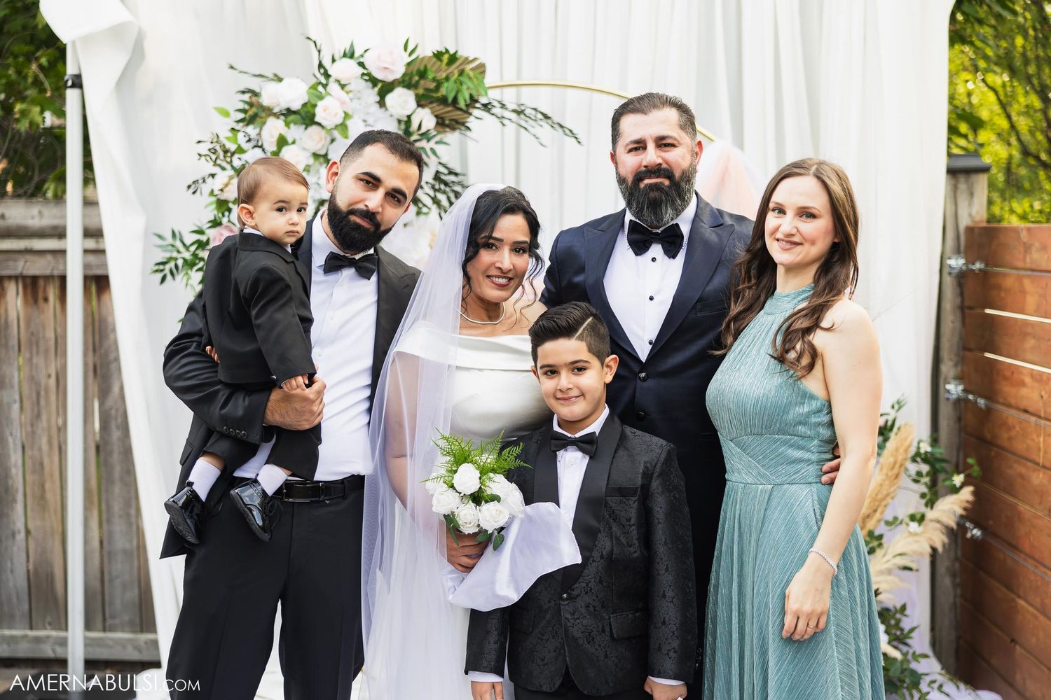 Wedding party portrait in front of white backdrop with floral decor.