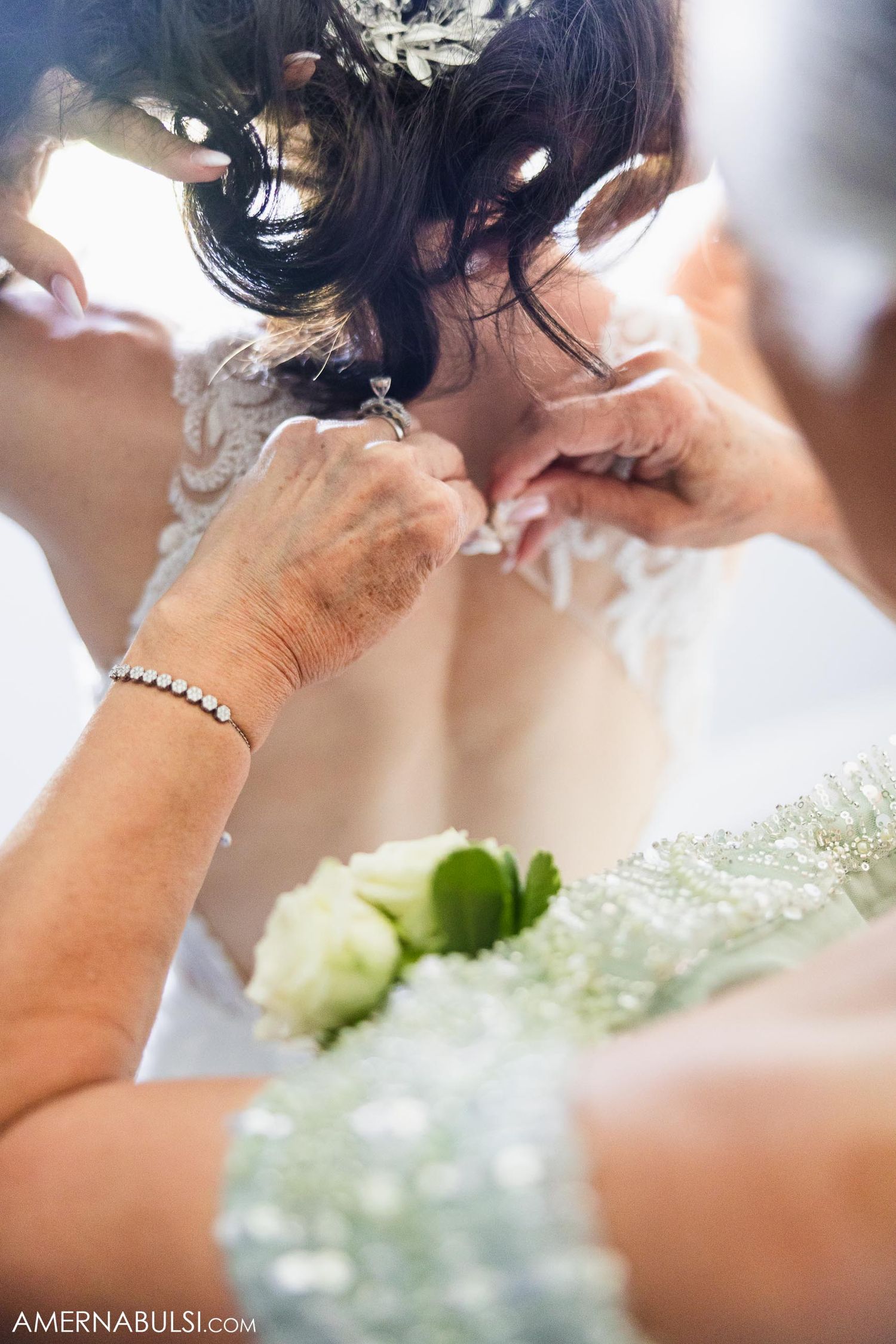 Close-up detail shot of hands adjusting wedding dress details with flowers in foreground.