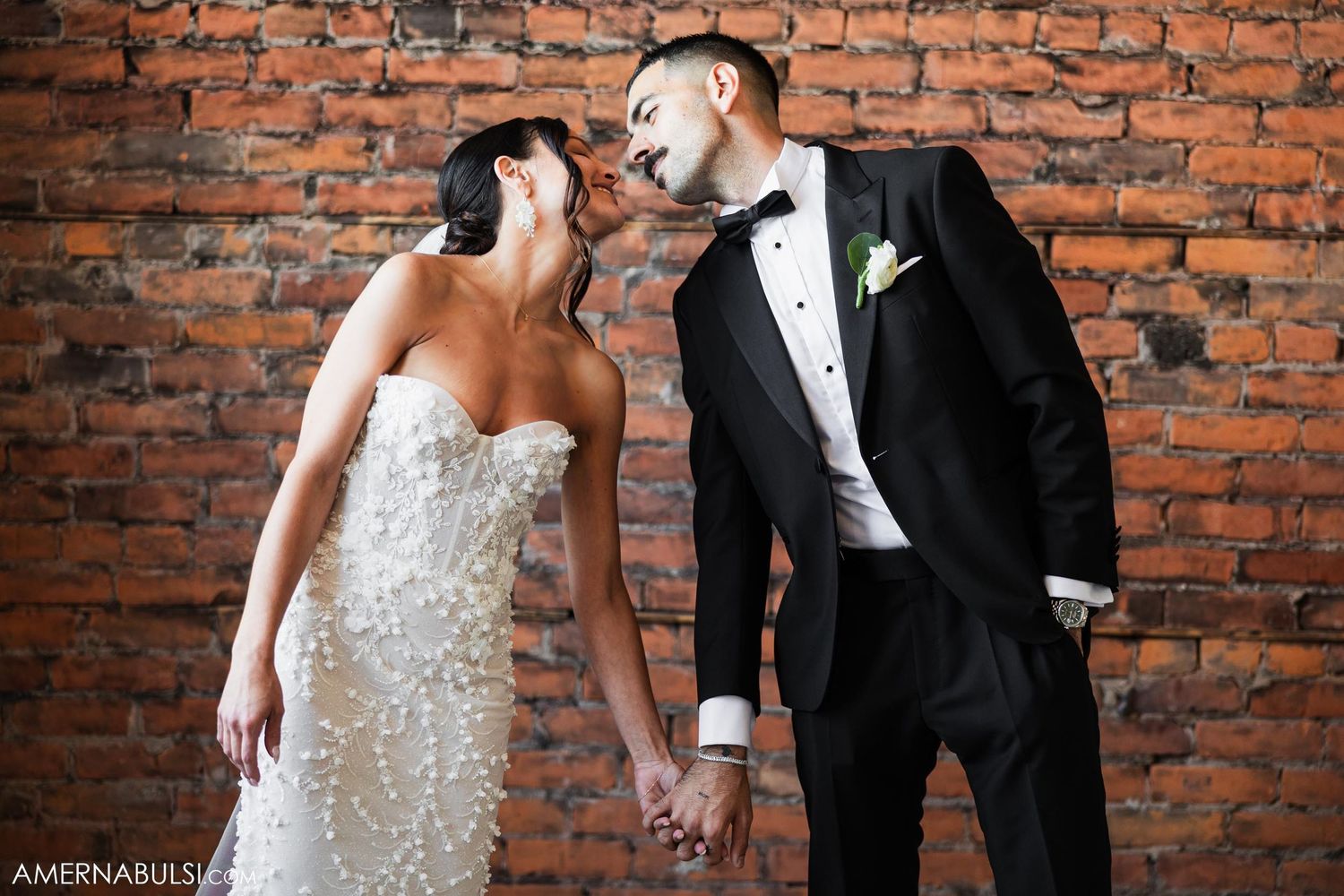 Romantic moment between newlyweds against an exposed brick wall.