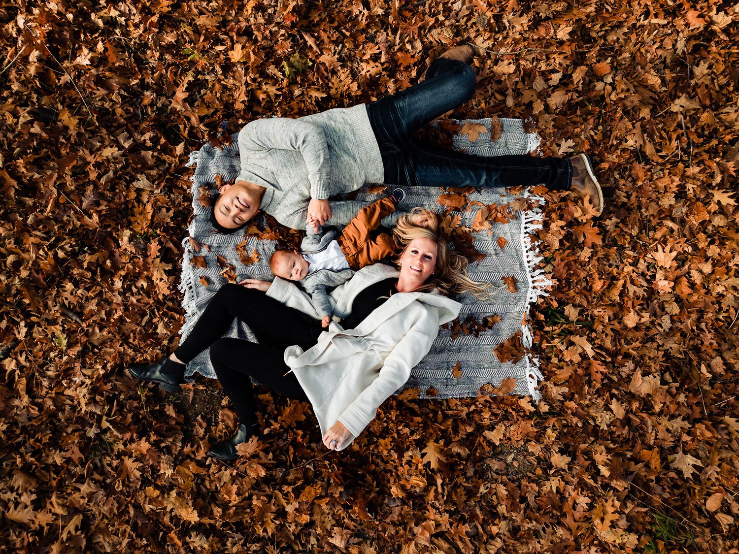 People lying in scattered autumn leaves creating artistic poses on the ground.