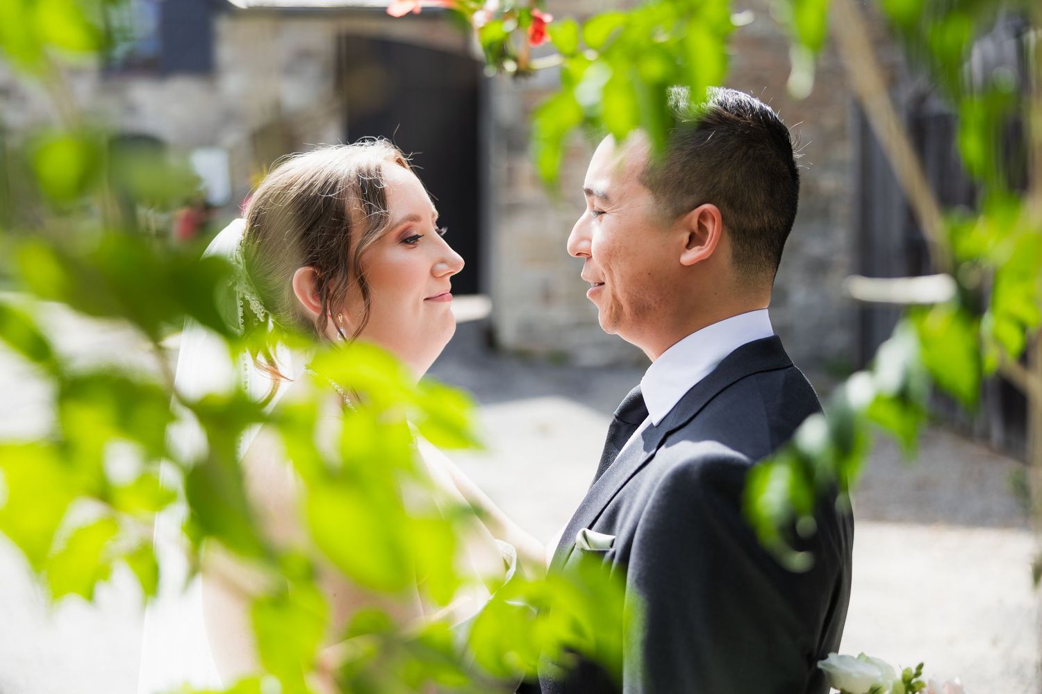 Bride and groom share an intimate moment surrounded by lush green foliage at their outdoor wedding ceremony.