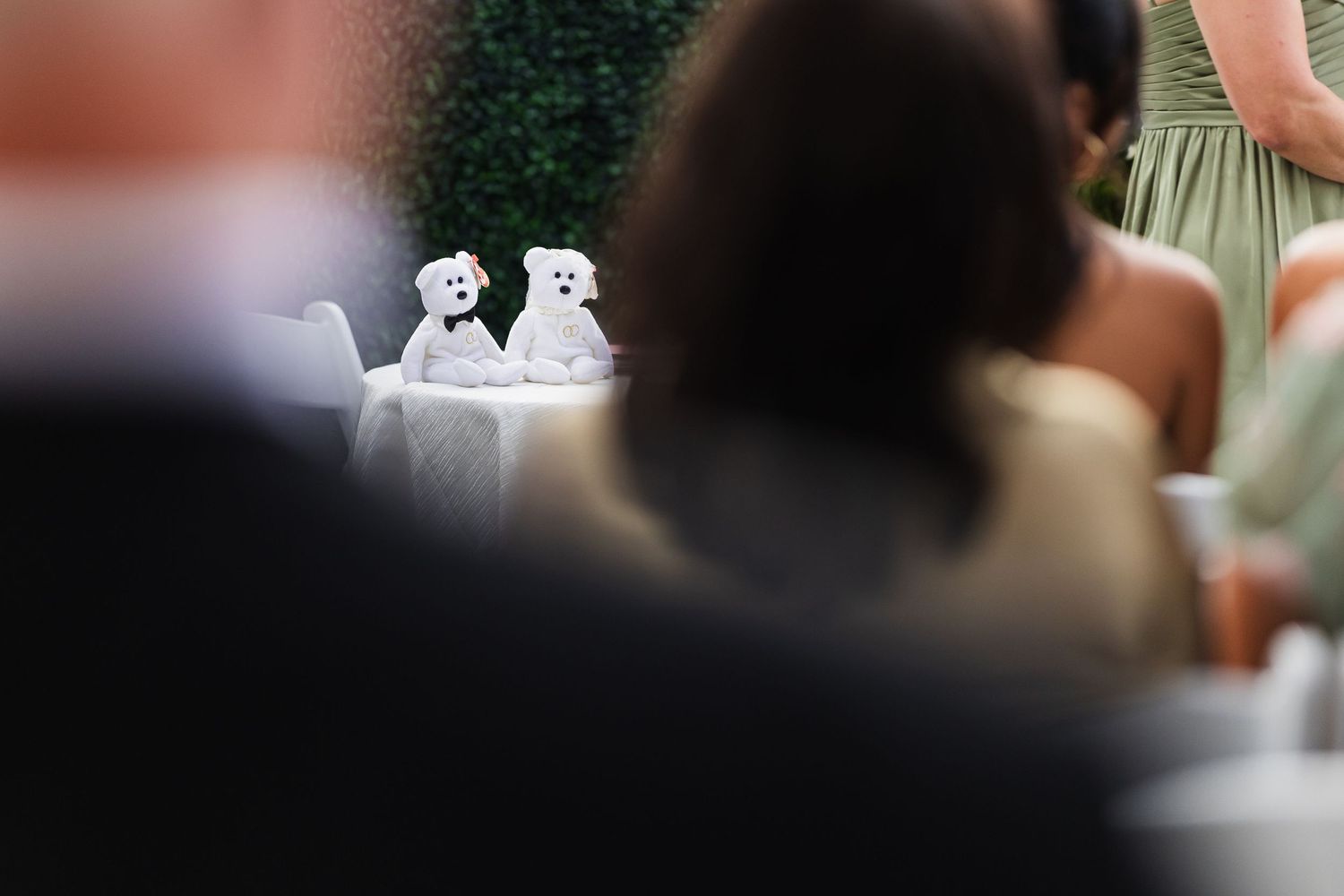 Two white teddy bear wedding cake toppers displayed on a table at a wedding reception.