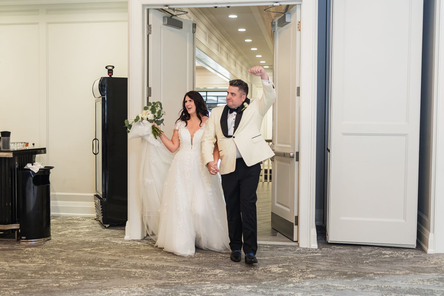 Bride and groom make grand entrance into wedding reception hall, bride in white ballgown holding bouquet.