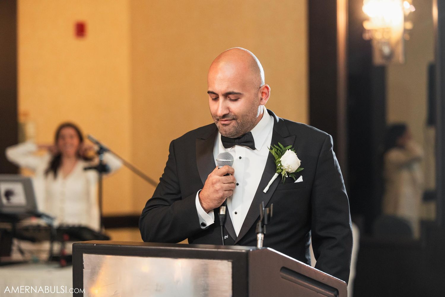 Speaker in tuxedo delivers heartfelt speech at wedding reception podium.