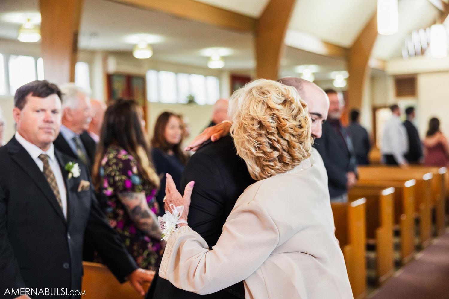 Wedding guests stand in church pews during a ceremony while others share a joyful moment.