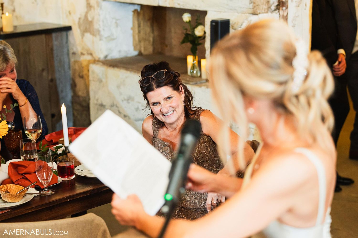 Wedding guests share laughter while reading at a reception dinner table.
