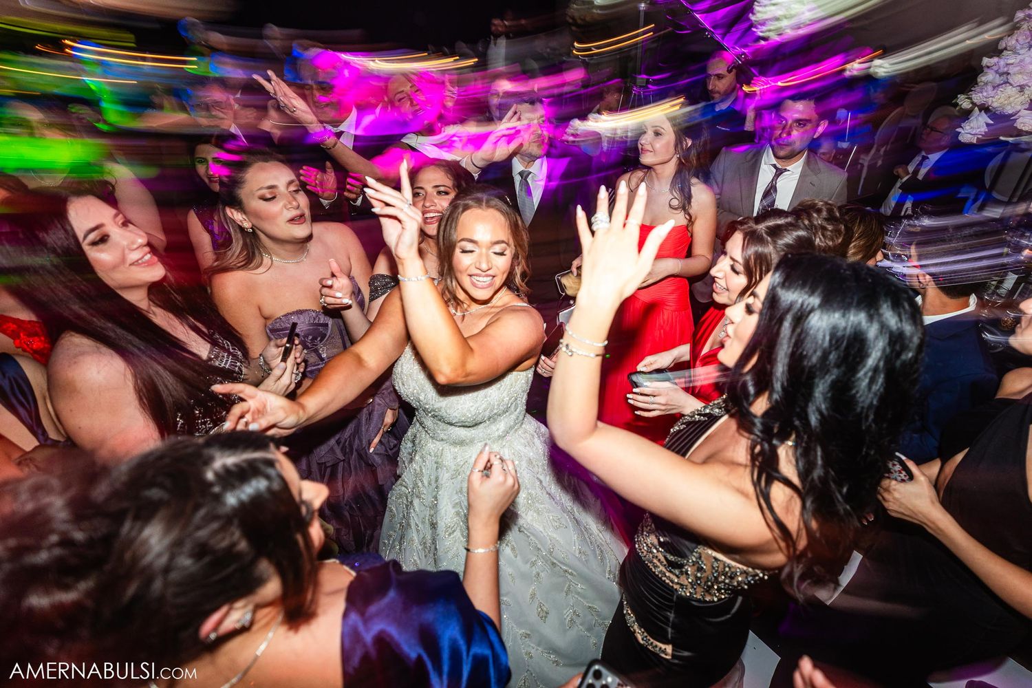 Guests celebrate in formal attire on a dance floor illuminated by colorful lights and motion blur effects.