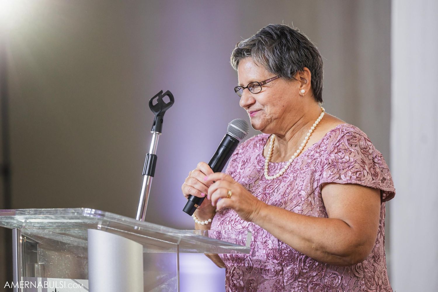 A person in pink dress speaking at a podium during a formal event.
