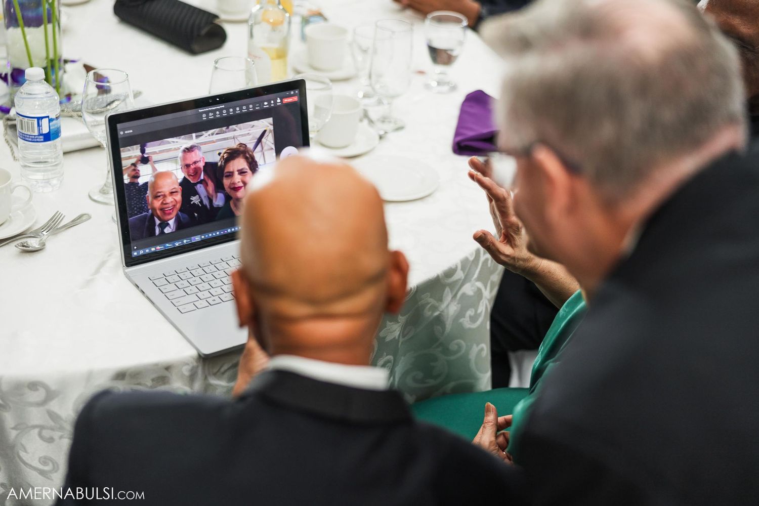 Wedding guests watching presentation on laptop during reception dinner.