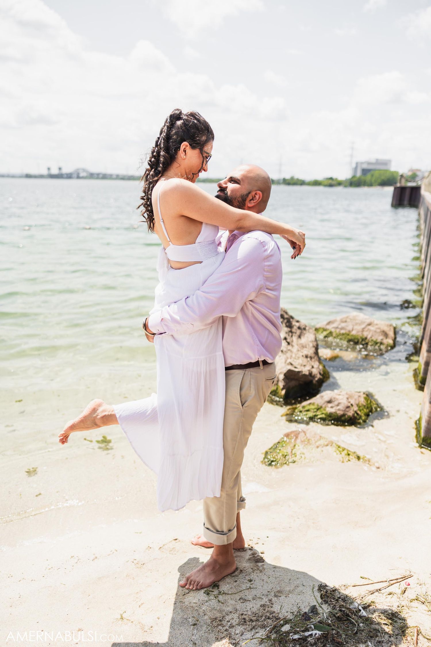 Joyful couple embracing on beach rocks with water in background.