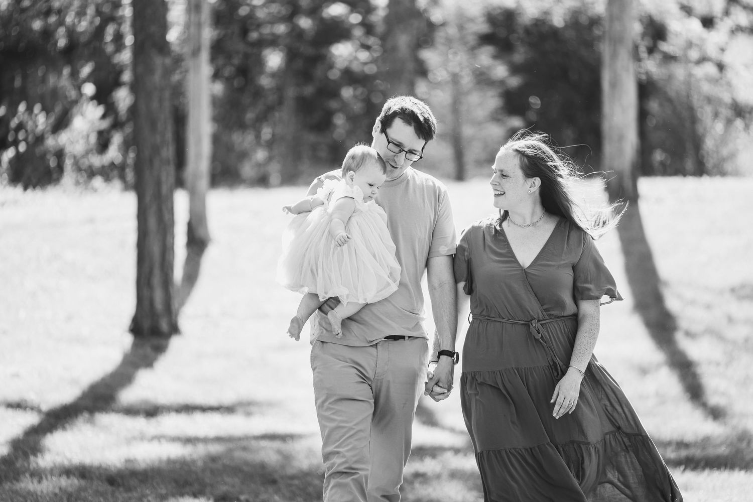 Black and white photo of family walking together through sunlit forest.