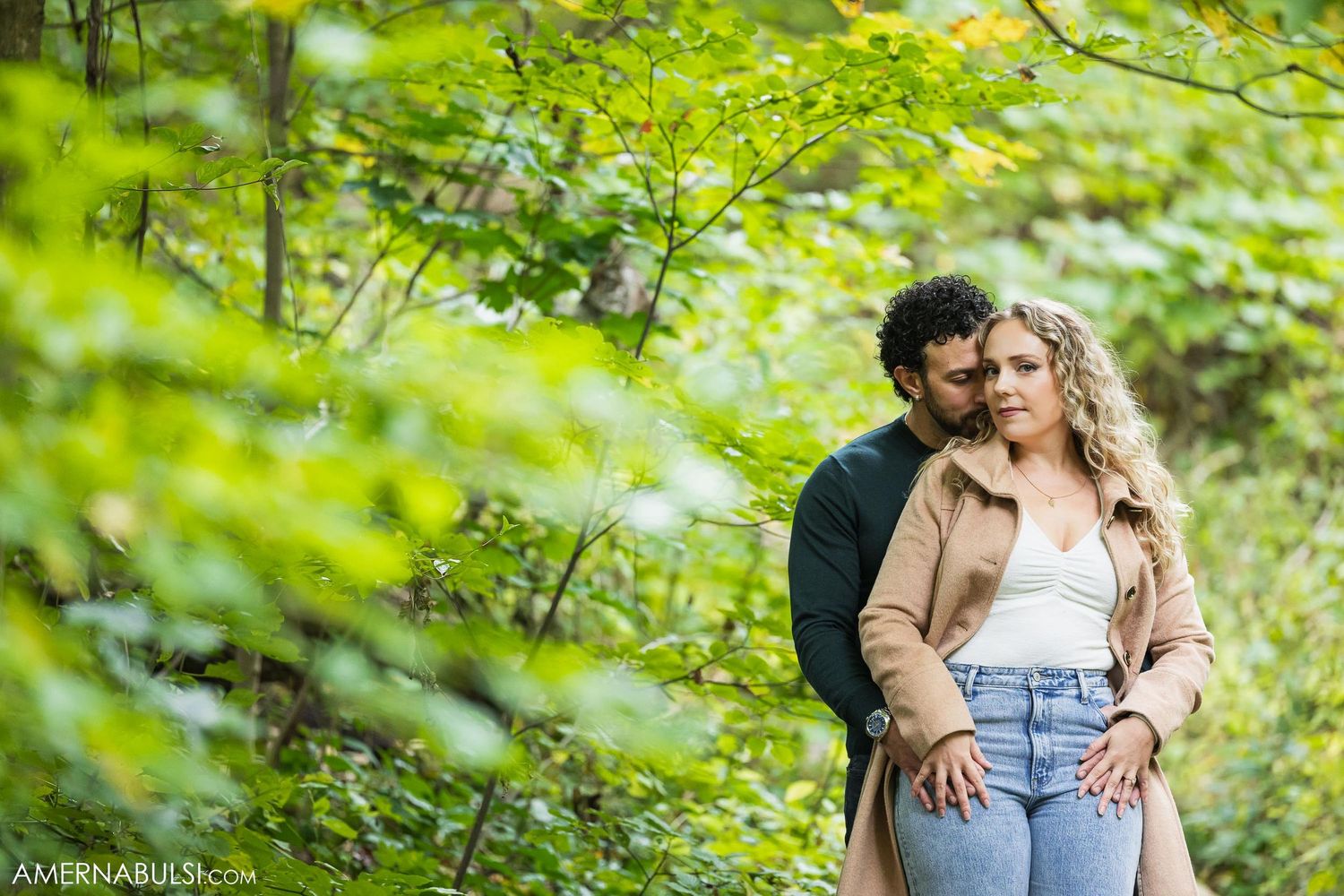 A romantic couple poses together in a lush green forest setting during a photo session.