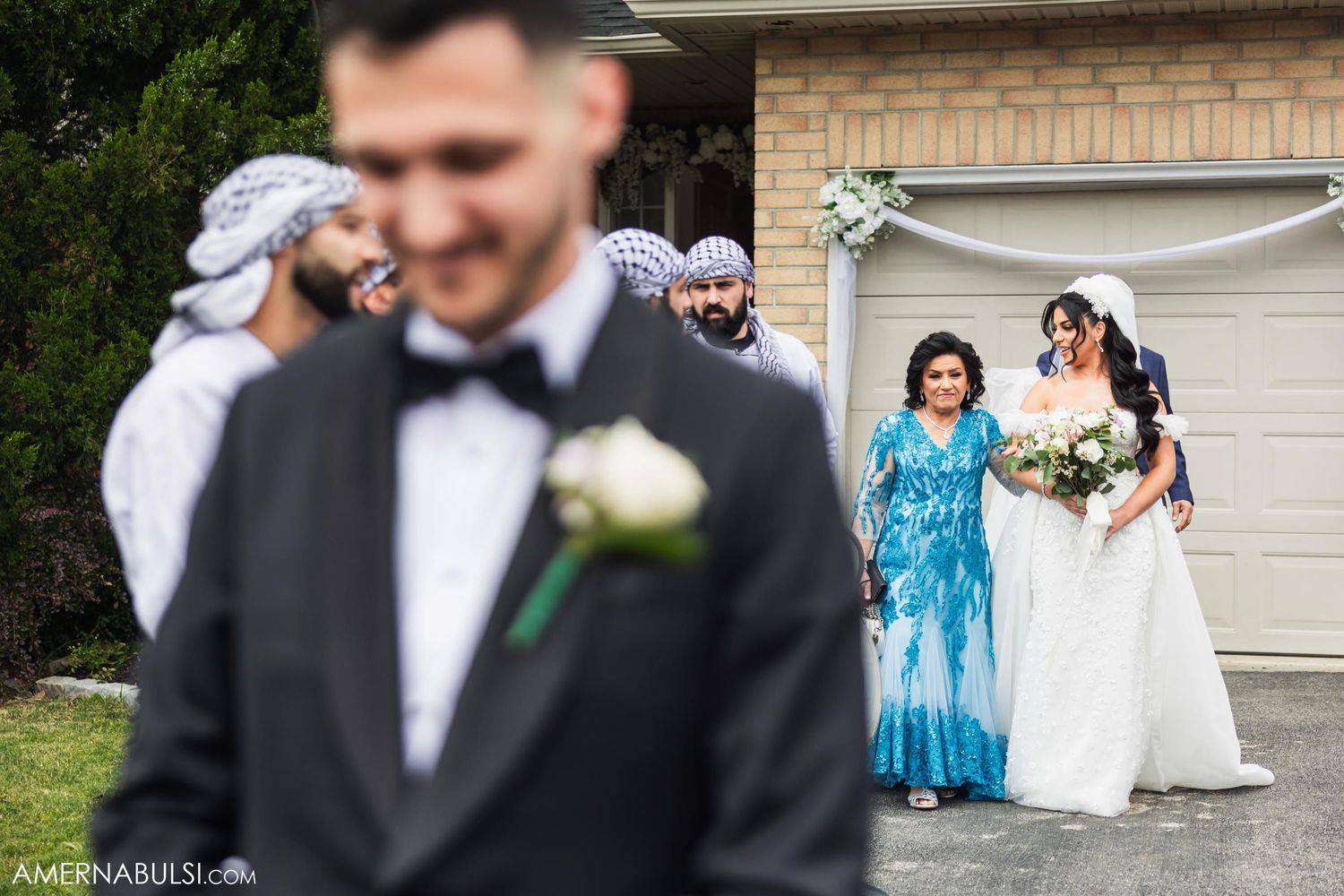 Wedding party and family members watch the couple's first look from the driveway.