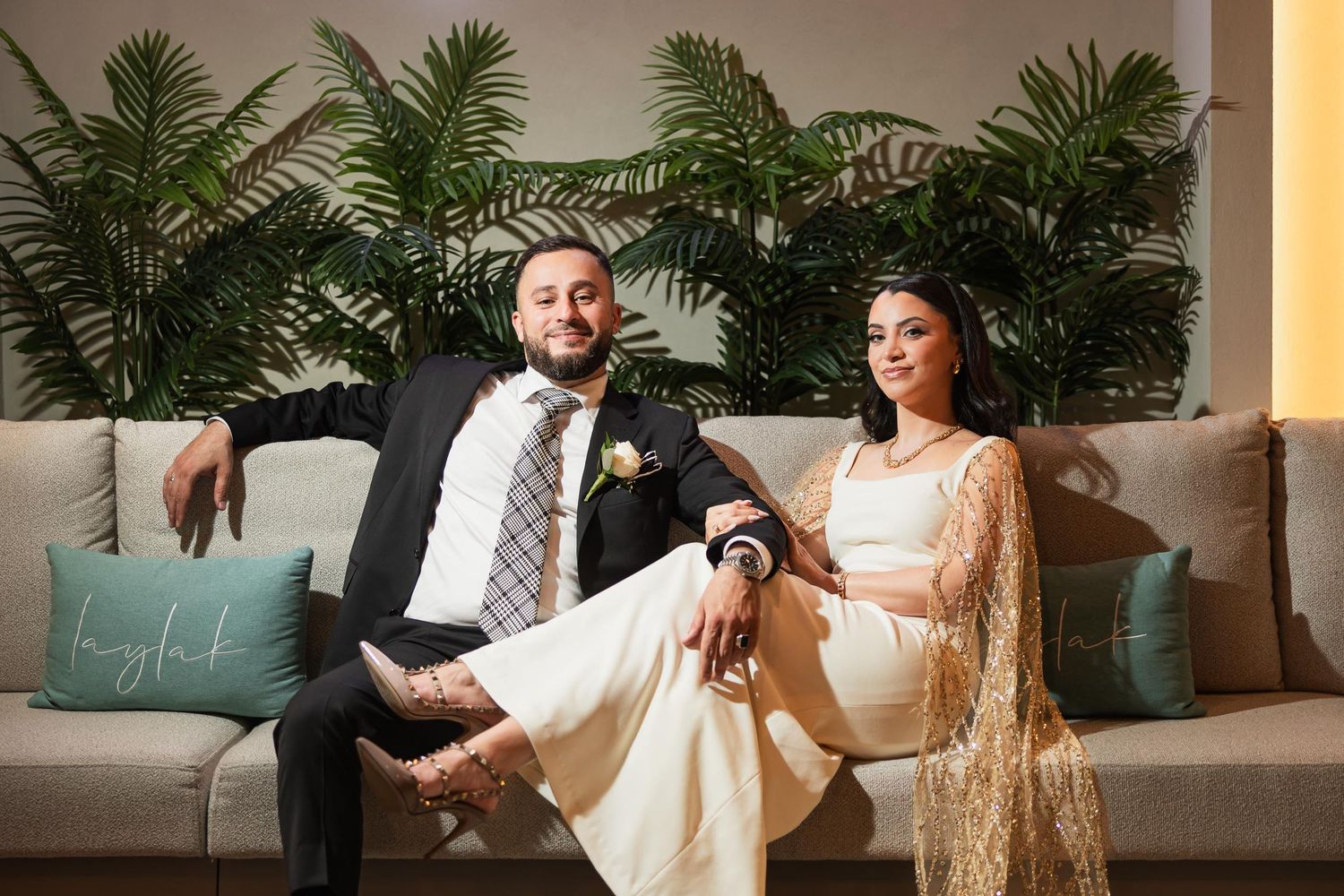 Relaxed couple pose on modern couch with tropical palm decor.