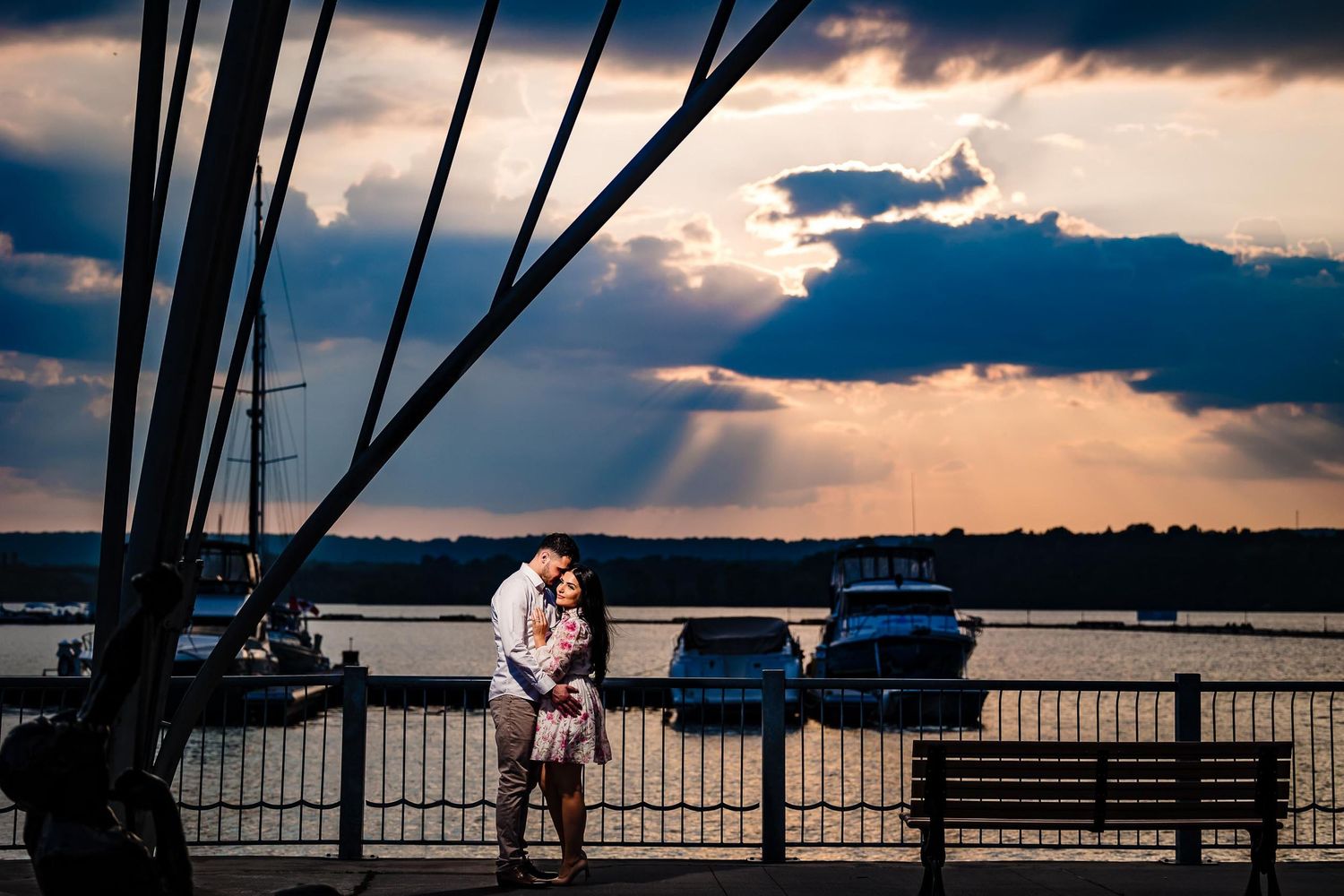 Silhouetted couple embracing at waterfront during dramatic sunset.