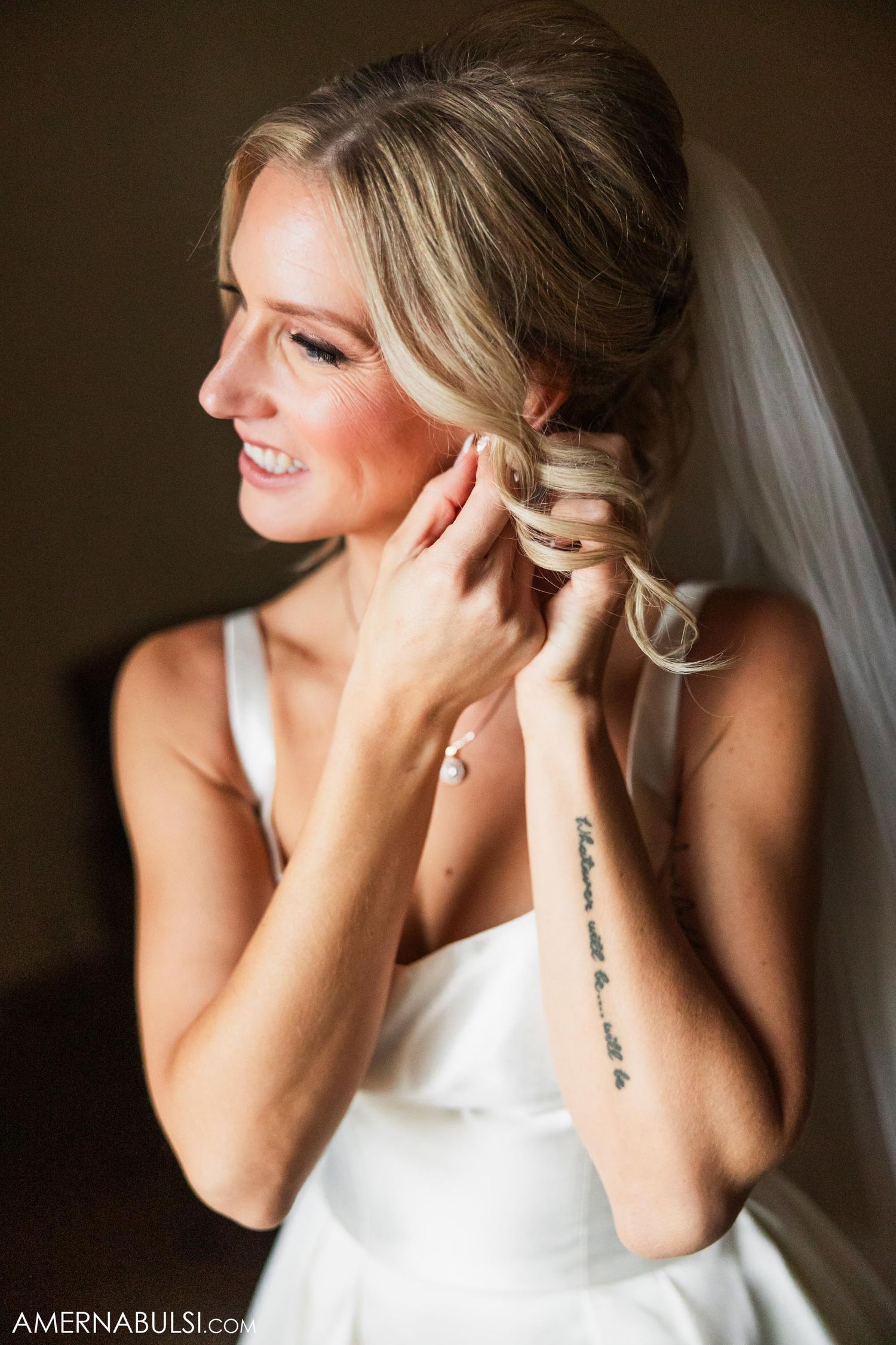 A bride in white dress puts on earrings while getting ready.