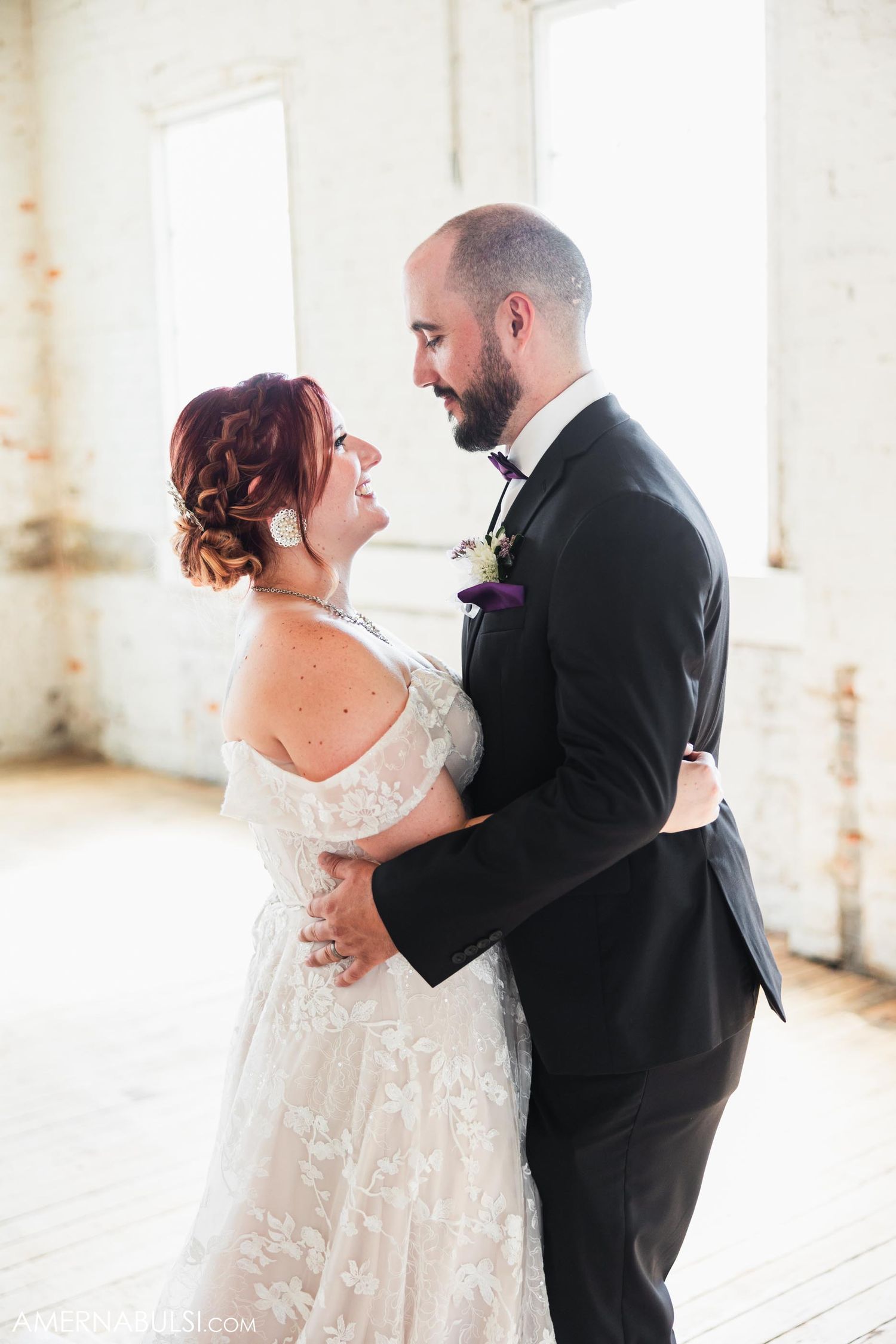 Romantic wedding portrait in bright sunlit industrial room with white walls.